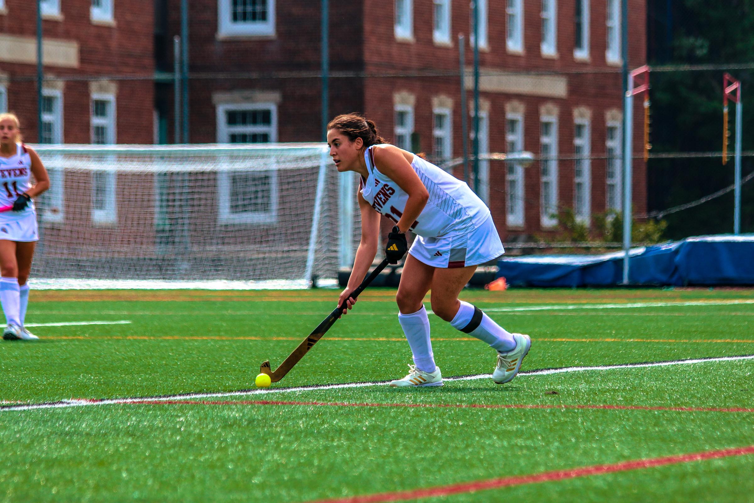 Emilia runs on the field with the ball while playing field hockey