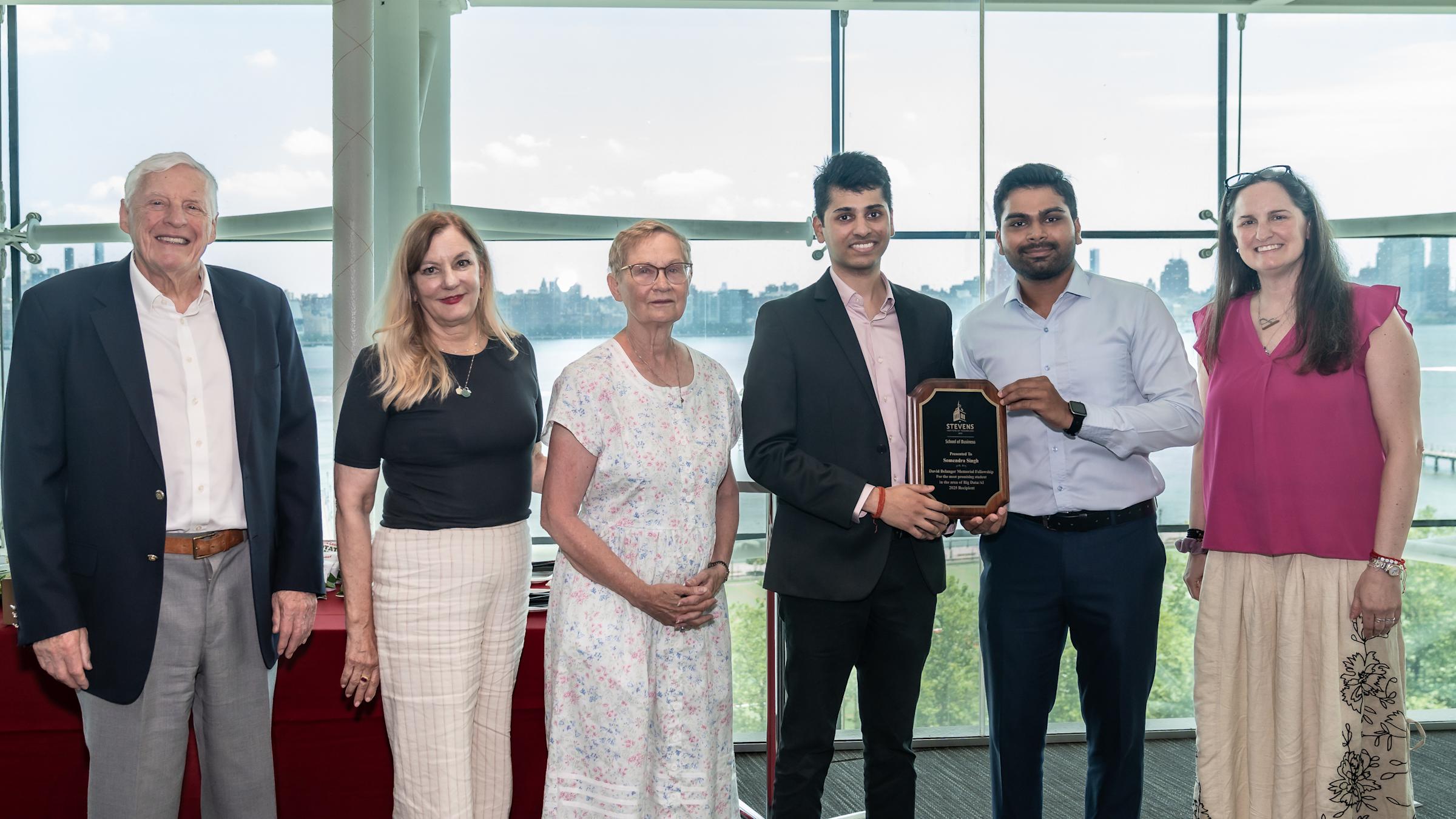 Six people pose in a modern office with city views. Two young men in business attire hold an award plaque, flanked by four others including an older man in a blazer, women in professional dress, celebrating the award.