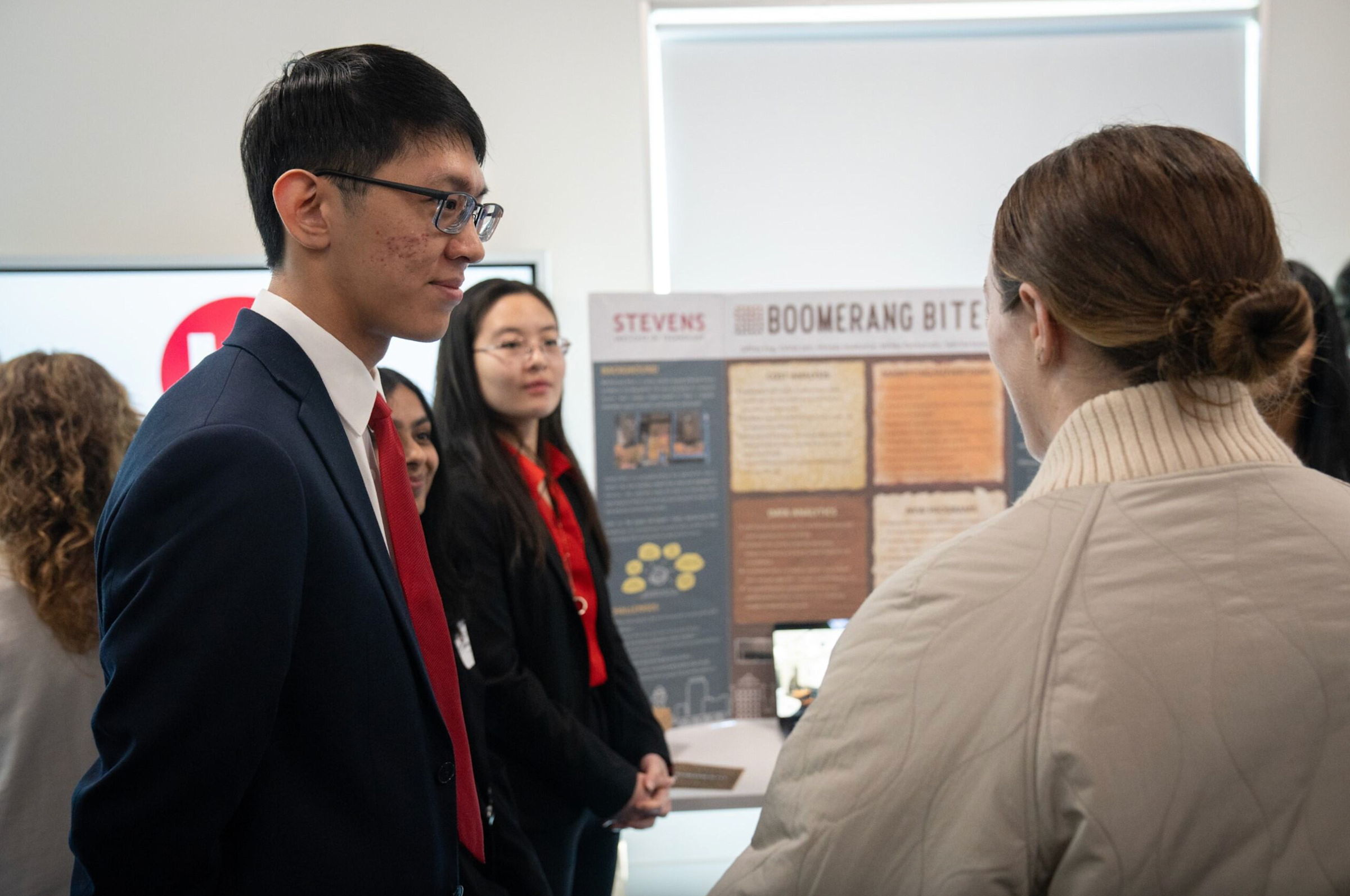 A member of the Boomerang Bites team in a blue blazer and red tie talks with a woman in front of their project.
