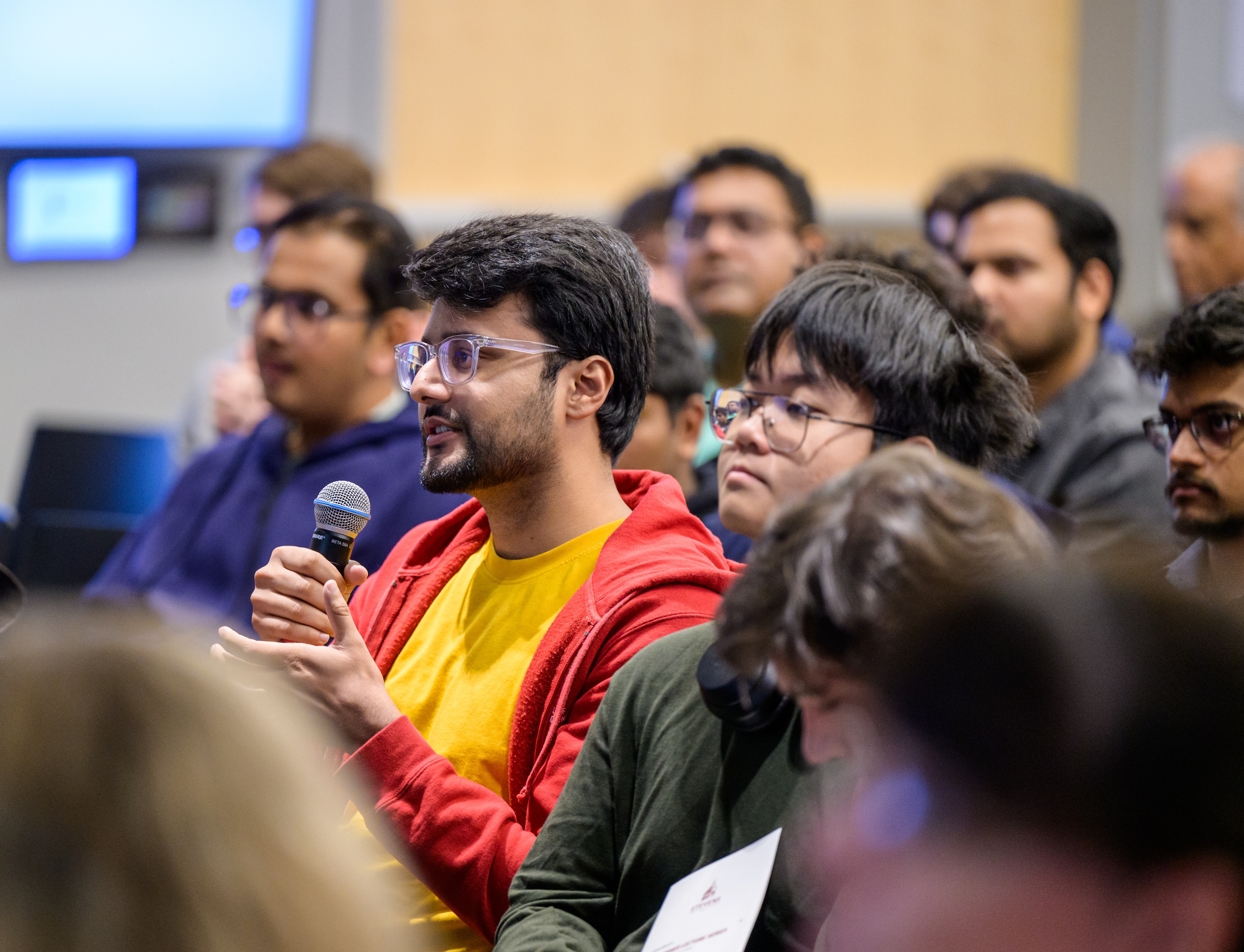 A male audience member seated among other members, holding a microphone.