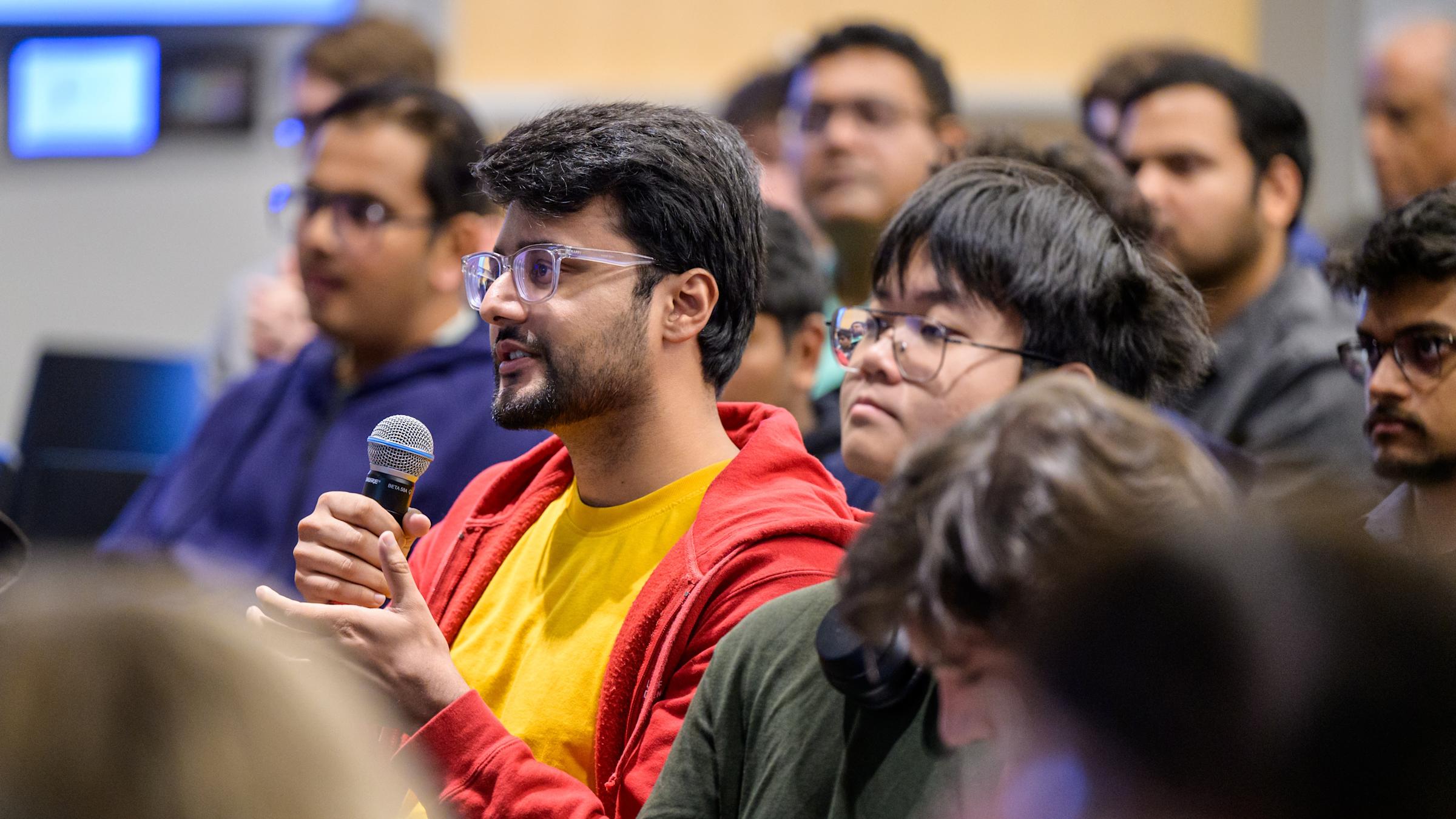 A male audience member seated among other members, holding a microphone.