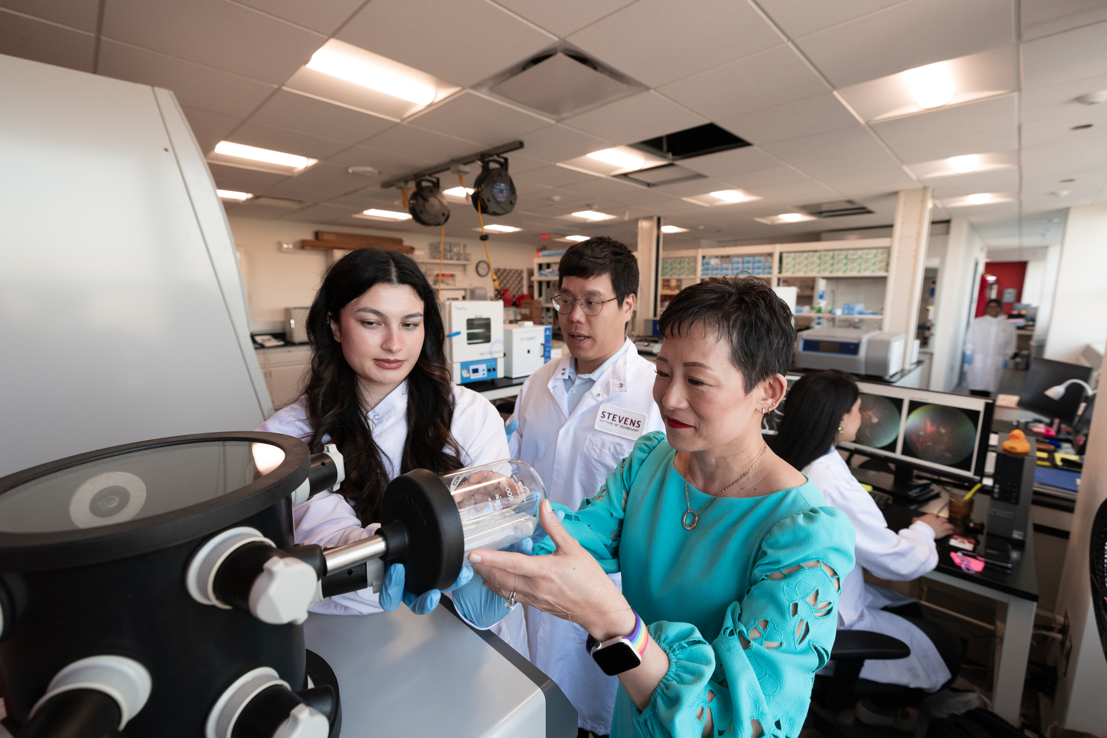 Jennifer Kang-Mieler on the right and two research students to her left looking at a microscope.
