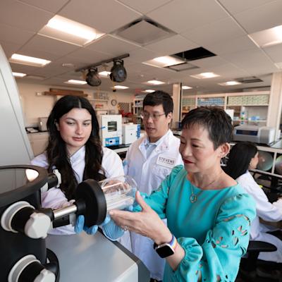 Jennifer Kang-Mieler on the right and two research students to her left looking at a microscope.