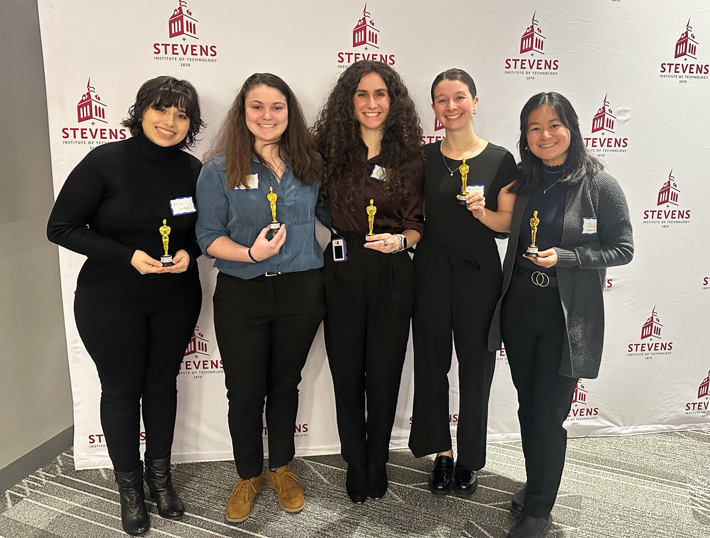 Students standing in front of Stevens event background holding trophies.