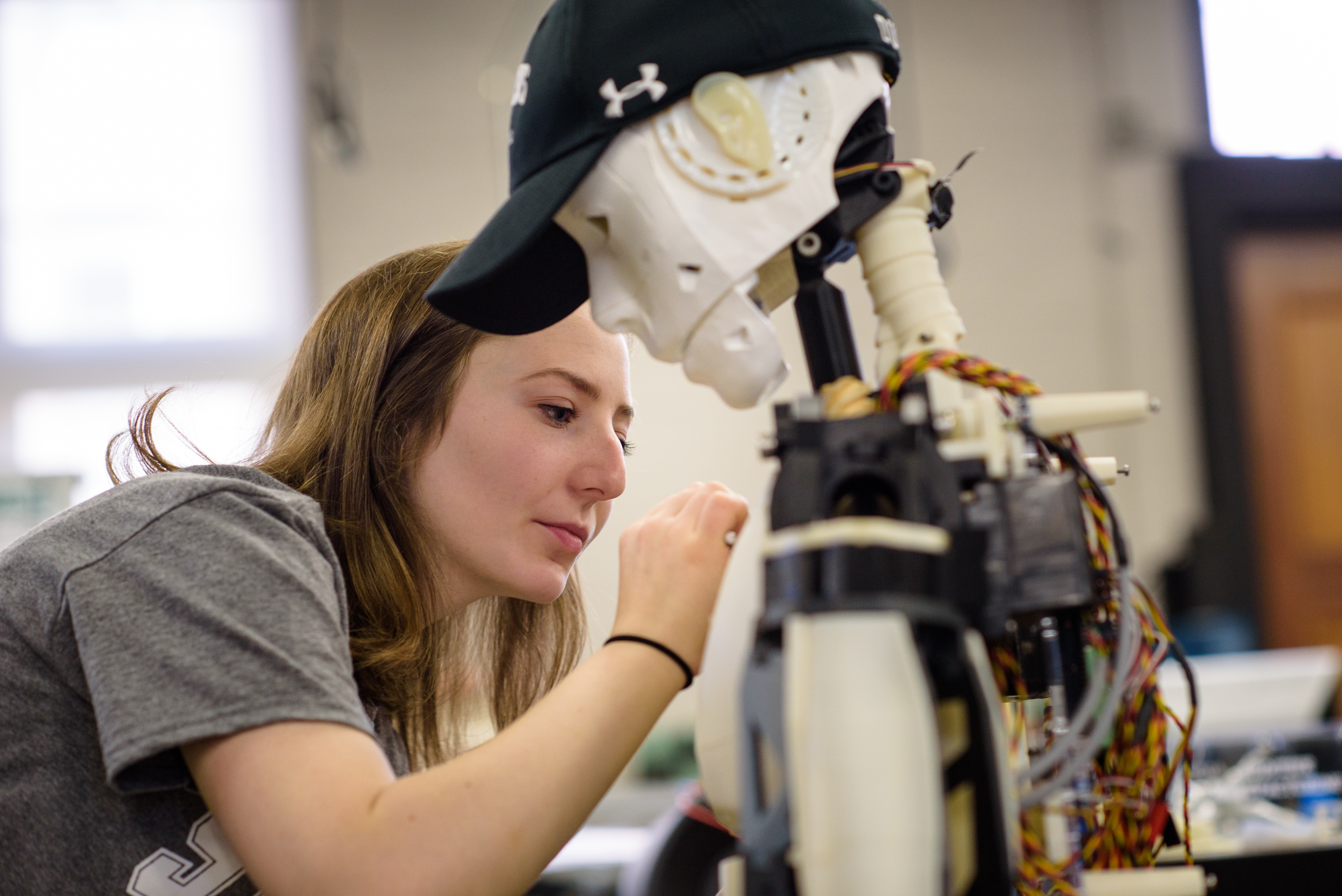 Student working on a white robot wearing a black Stevens hat with wires showing in its back