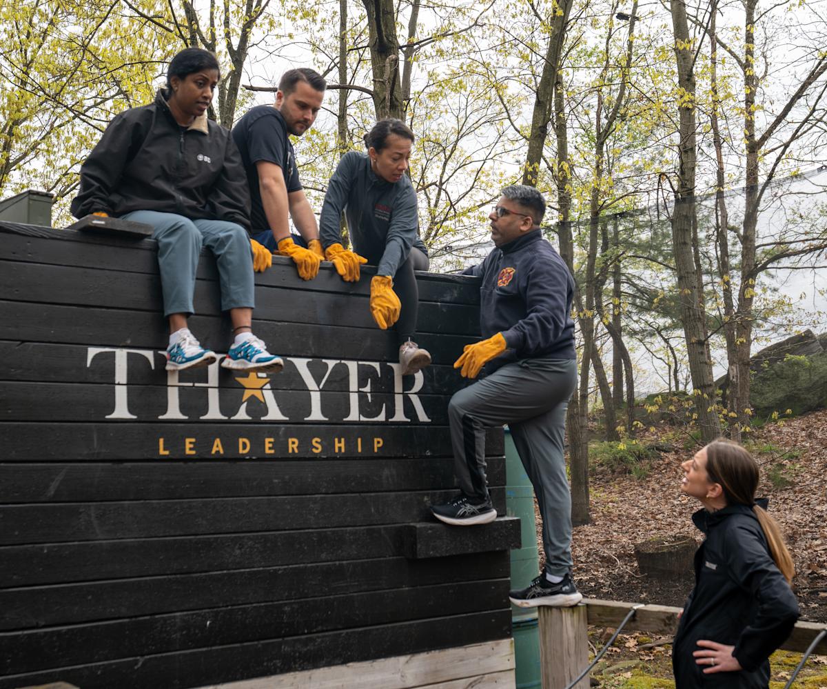 Four EMBA students sit on top of an obstacle course all with the Thayer Leadership logo discussing what their next move should be.