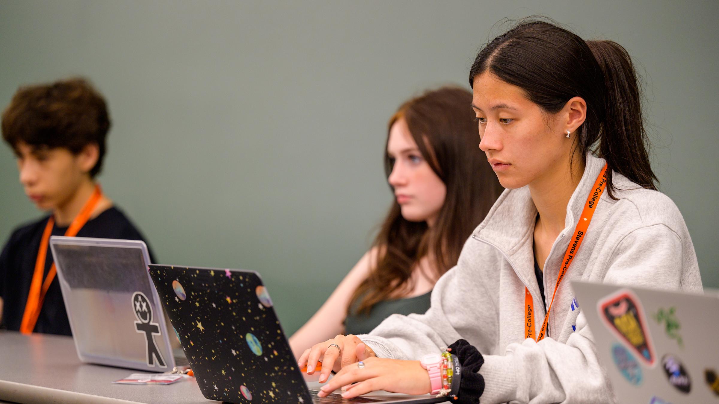 Student working on a laptop during class and 2 classmates use laptops in the background.