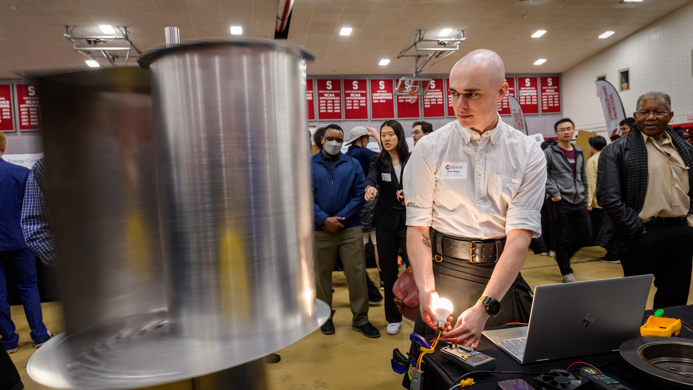 Student demonstrates his senior capstone project involving a metallic cylinder at Innovation Expo 2023 at Stevens.