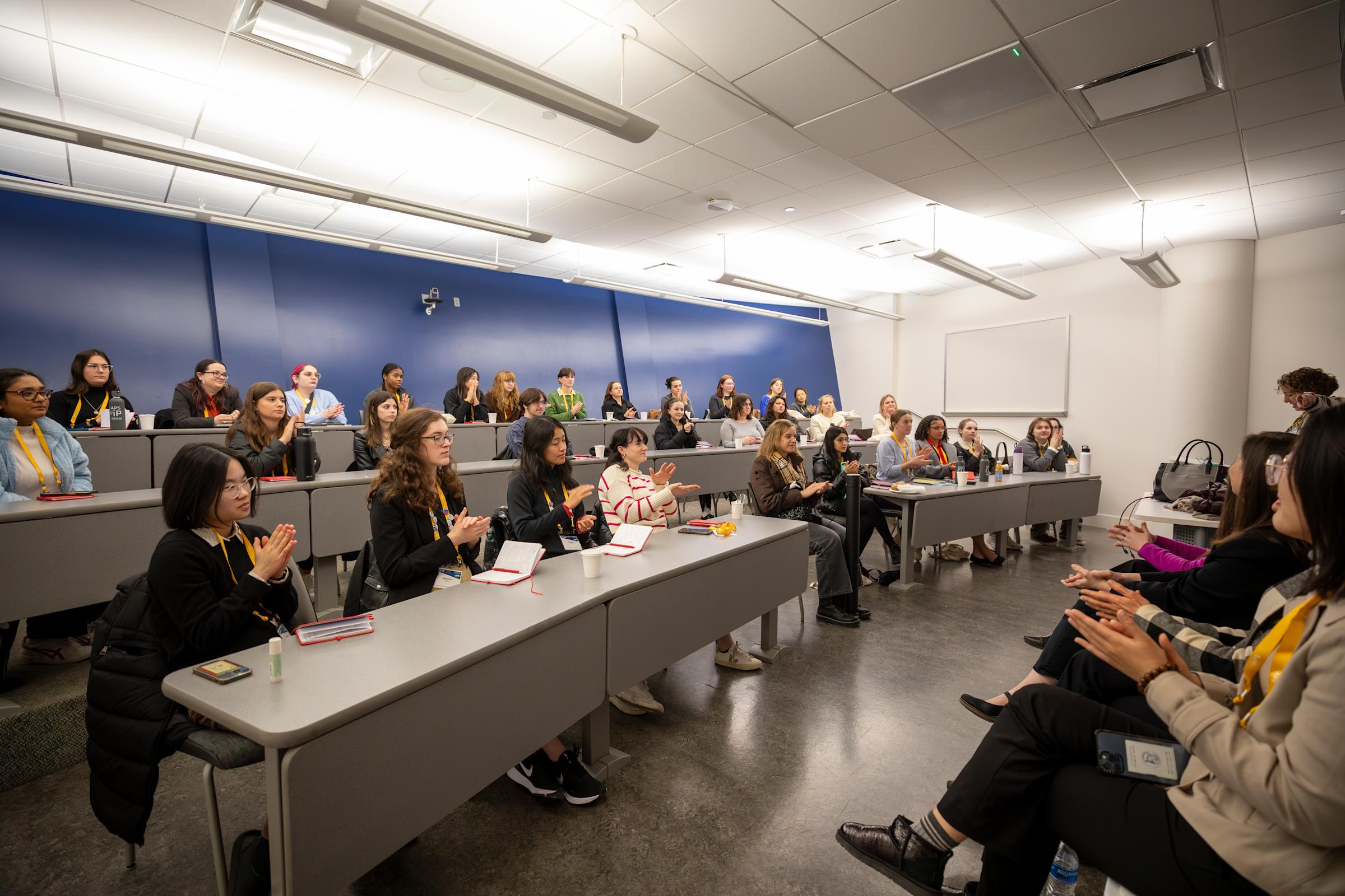 A group of CUWIP conference attendees seated in a classroom applaud during a workshop.