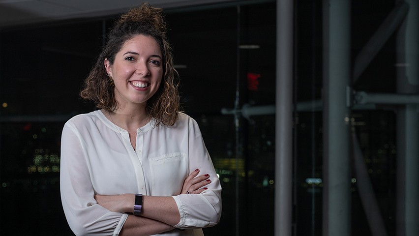Carolyn Cochran in a white blouse. The New York skyline is visible in the background.