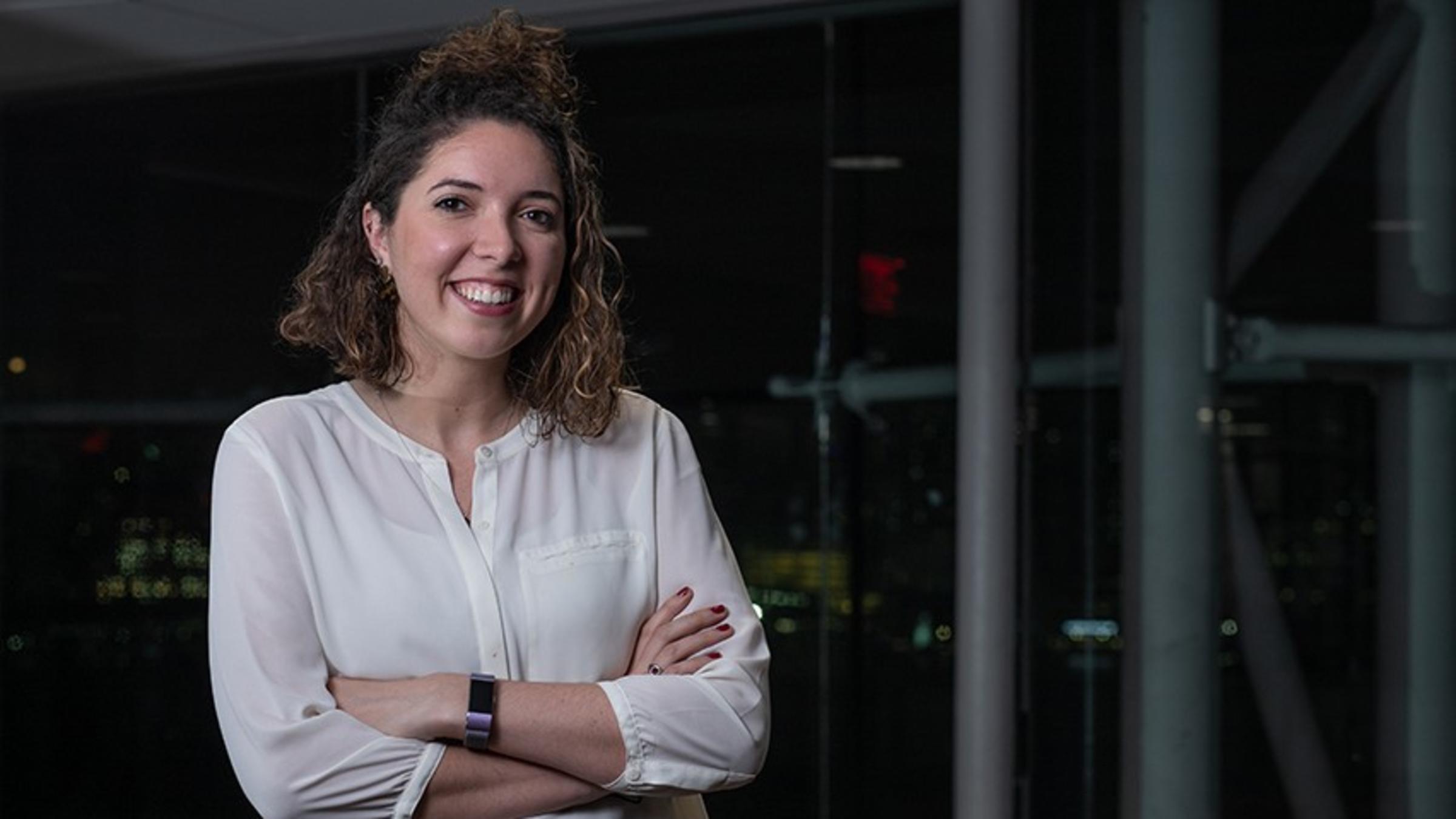 Carolyn Cochran in a white blouse. The New York skyline is visible in the background.