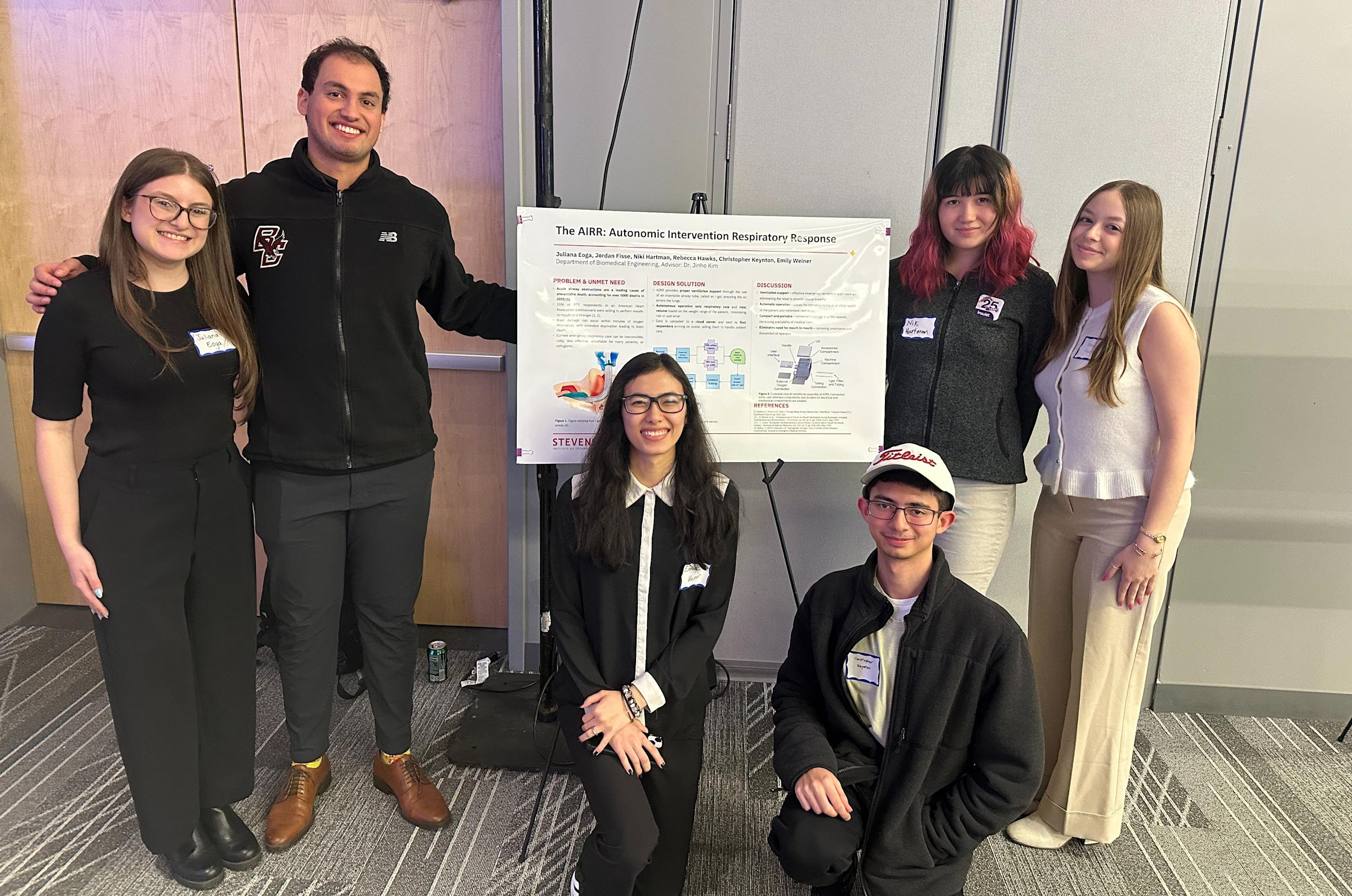 A group of six students, four women and two men, posing around their presentation poster for a photo.