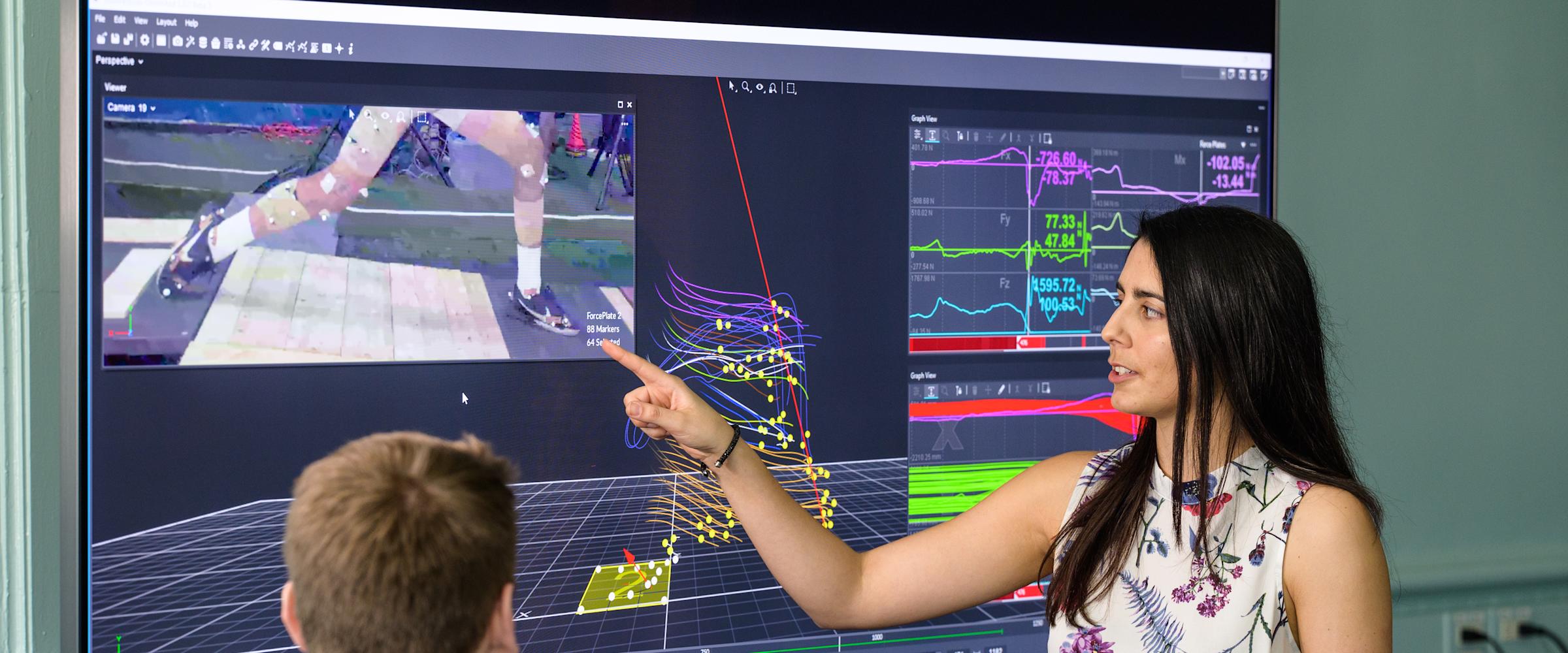 Instructor in front of monitor guides model outfitted in motion capture technology.