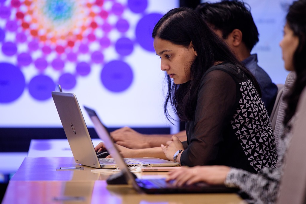 A student examines their laptop while a display screen lights up beside here at Stevens Center for Complex Systems and Enterprises Immersion Lab.