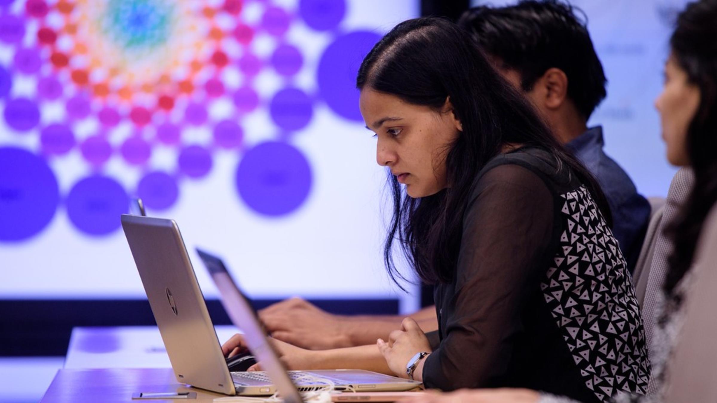 A student examines their laptop while a display screen lights up beside here at Stevens Center for Complex Systems and Enterprises Immersion Lab.