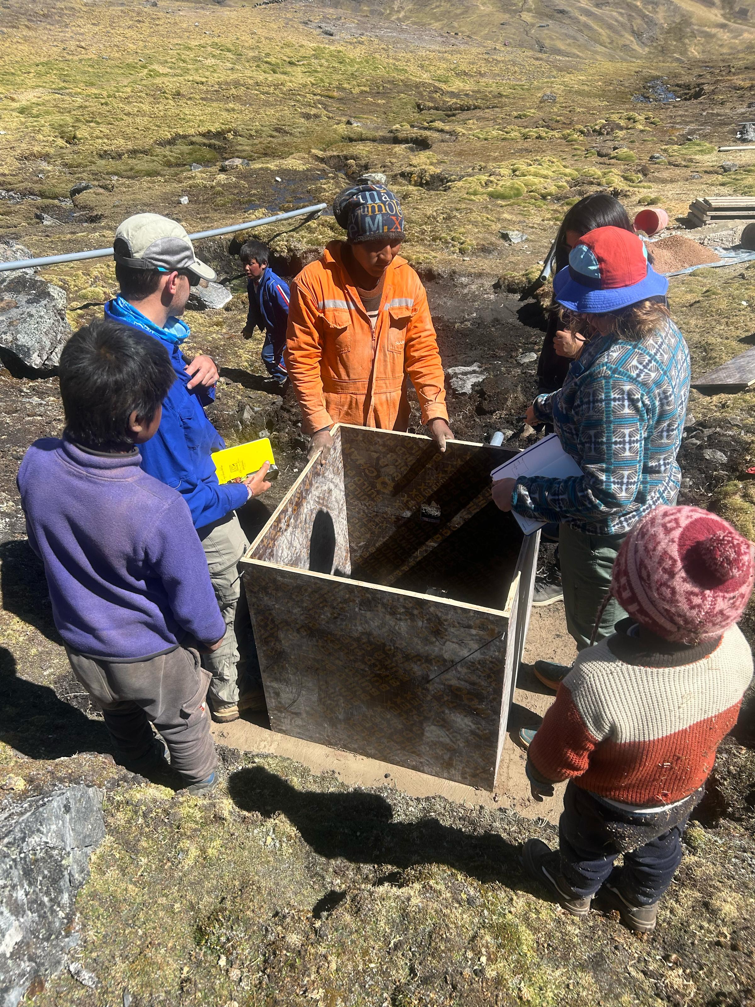 Students and community members gather around a box on a hillside.