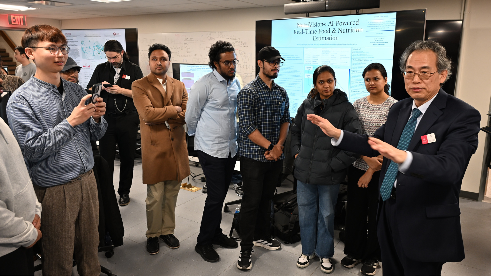 Department of Electrical and Computer Engineering chair Min Song addresses students at the iCNS AI Engineering and Science Symposium in a room in front of monitors displaying research.