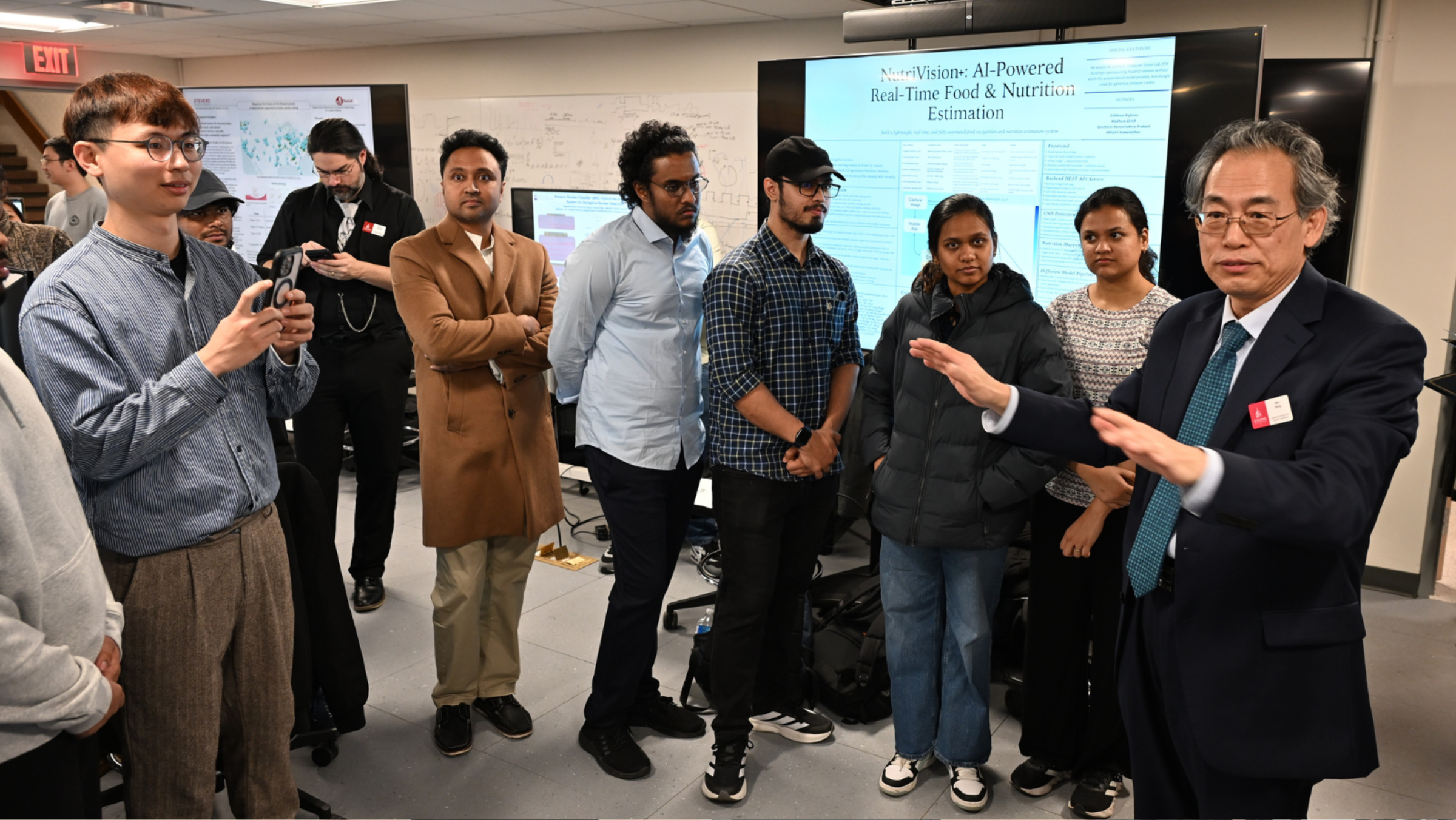 Department of Electrical and Computer Engineering chair Min Song addresses students at the iCNS AI Engineering and Science Symposium in a room in front of monitors displaying research.