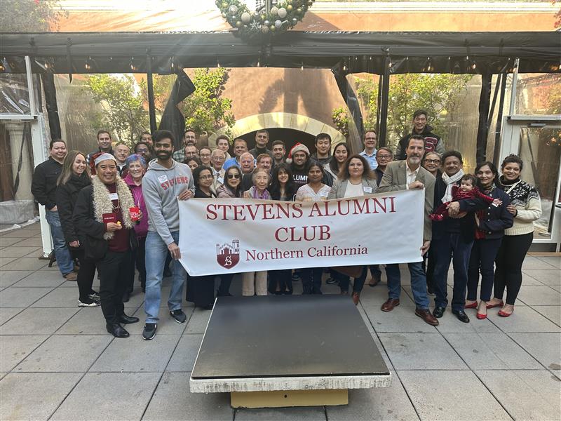 Attendees gather for a group photo at the Northern California Alumni Holiday Brunch 2025, holding a Stevens Alumni Club Northern California banner in an outdoor courtyard decorated with holiday greenery and seasonal décor.