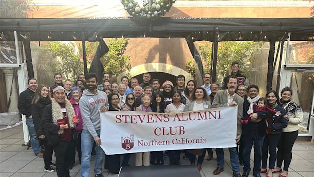 Attendees gather for a group photo at the Northern California Alumni Holiday Brunch 2025, holding a Stevens Alumni Club Northern California banner in an outdoor courtyard decorated with holiday greenery and seasonal décor.
