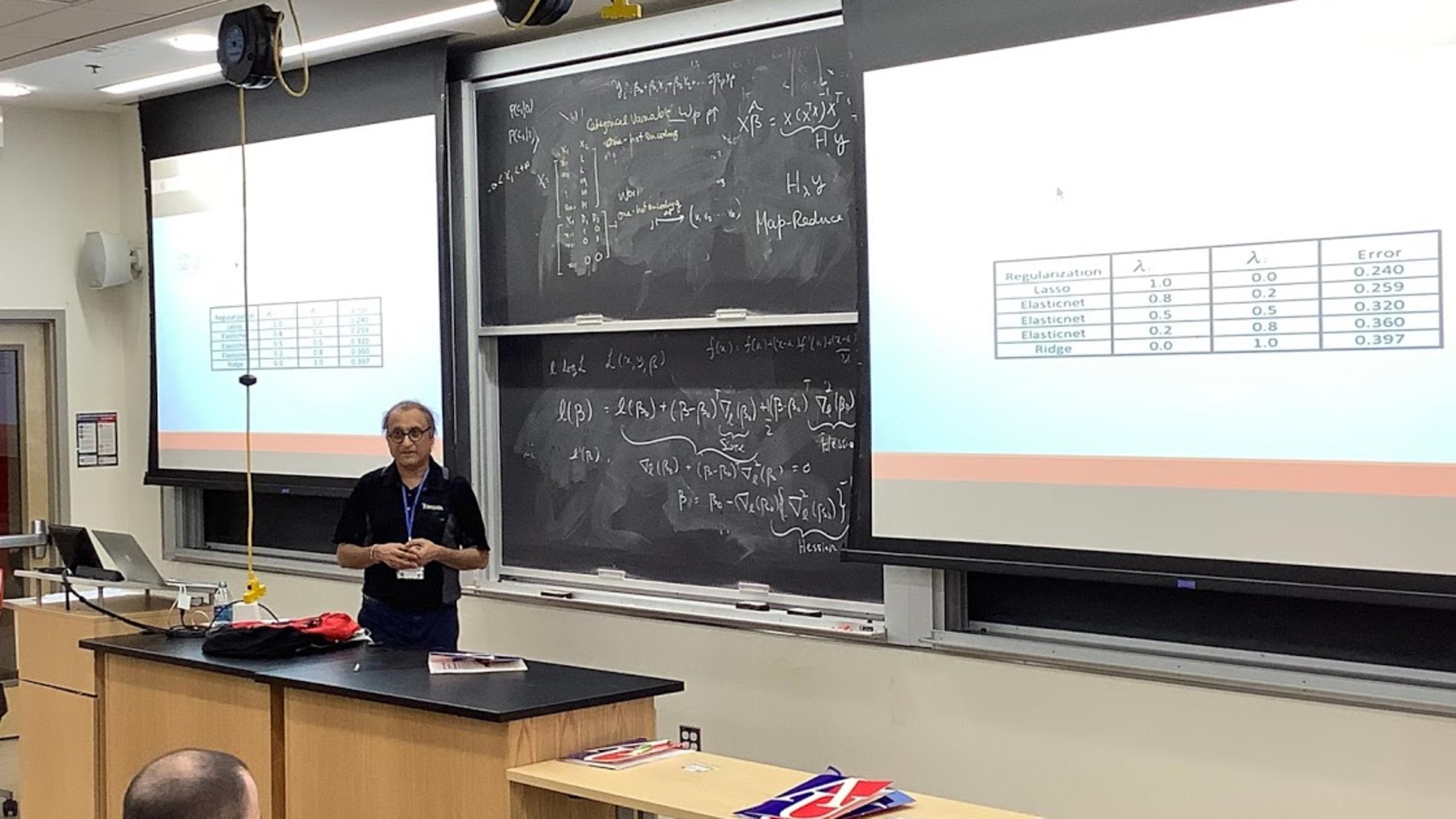 Choudur Lakshminarayan in front of a blackboard filled with statistical data.