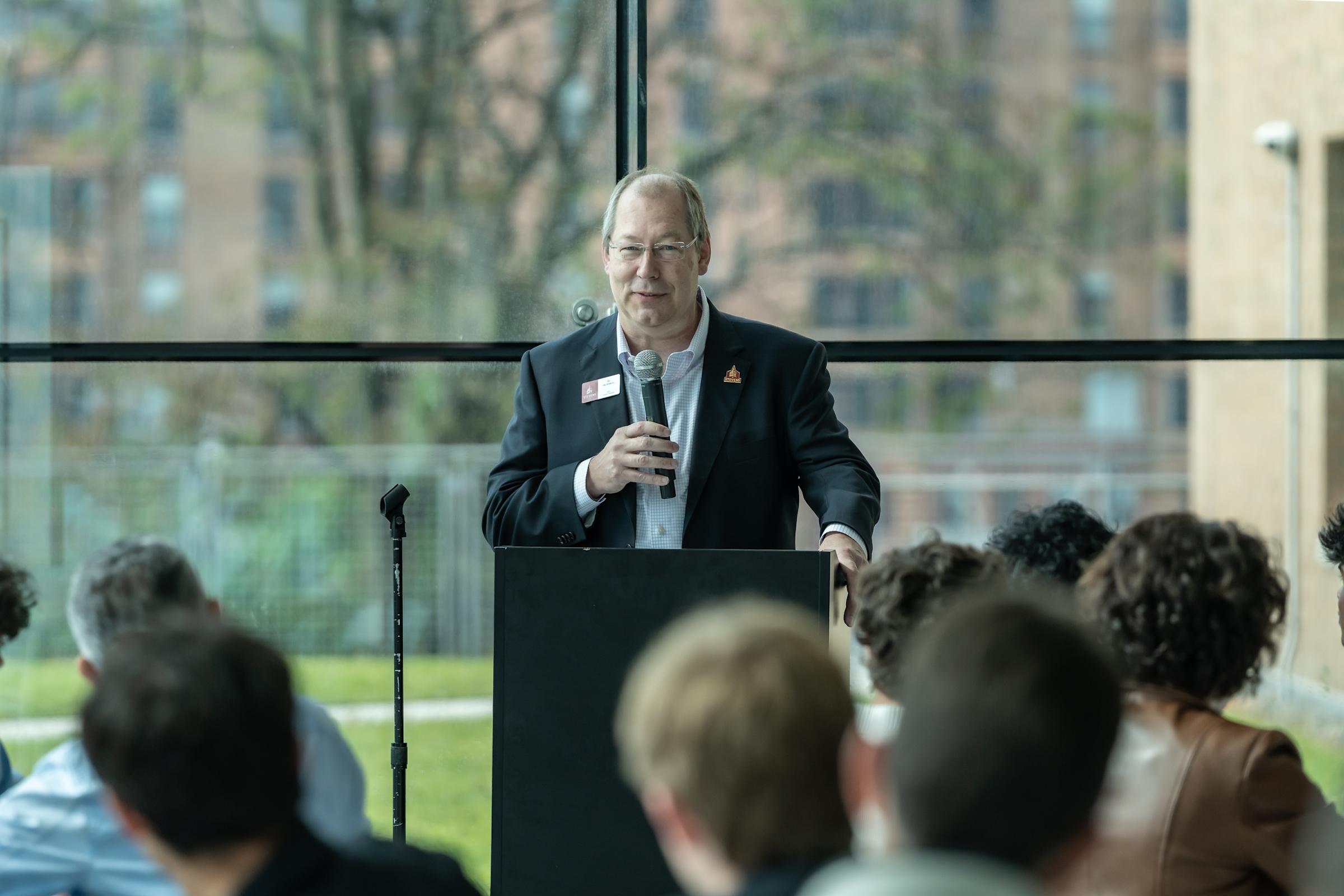 SSB Dean GJ de Vreede stands behind a podium holding a microphone.