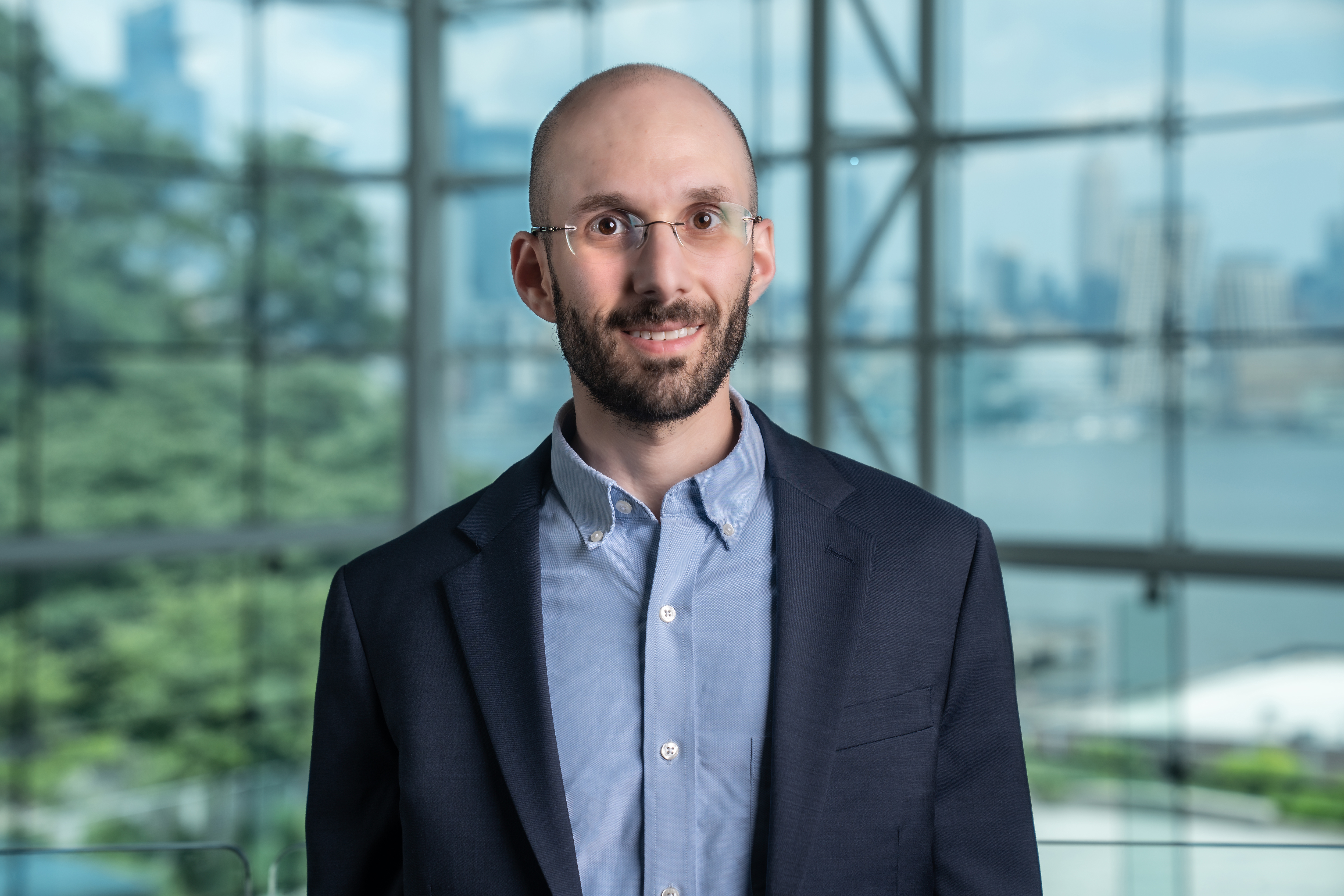 Zach Feinstein stands in the Babbio Center with the New York City skyline visible in the background through the windows.