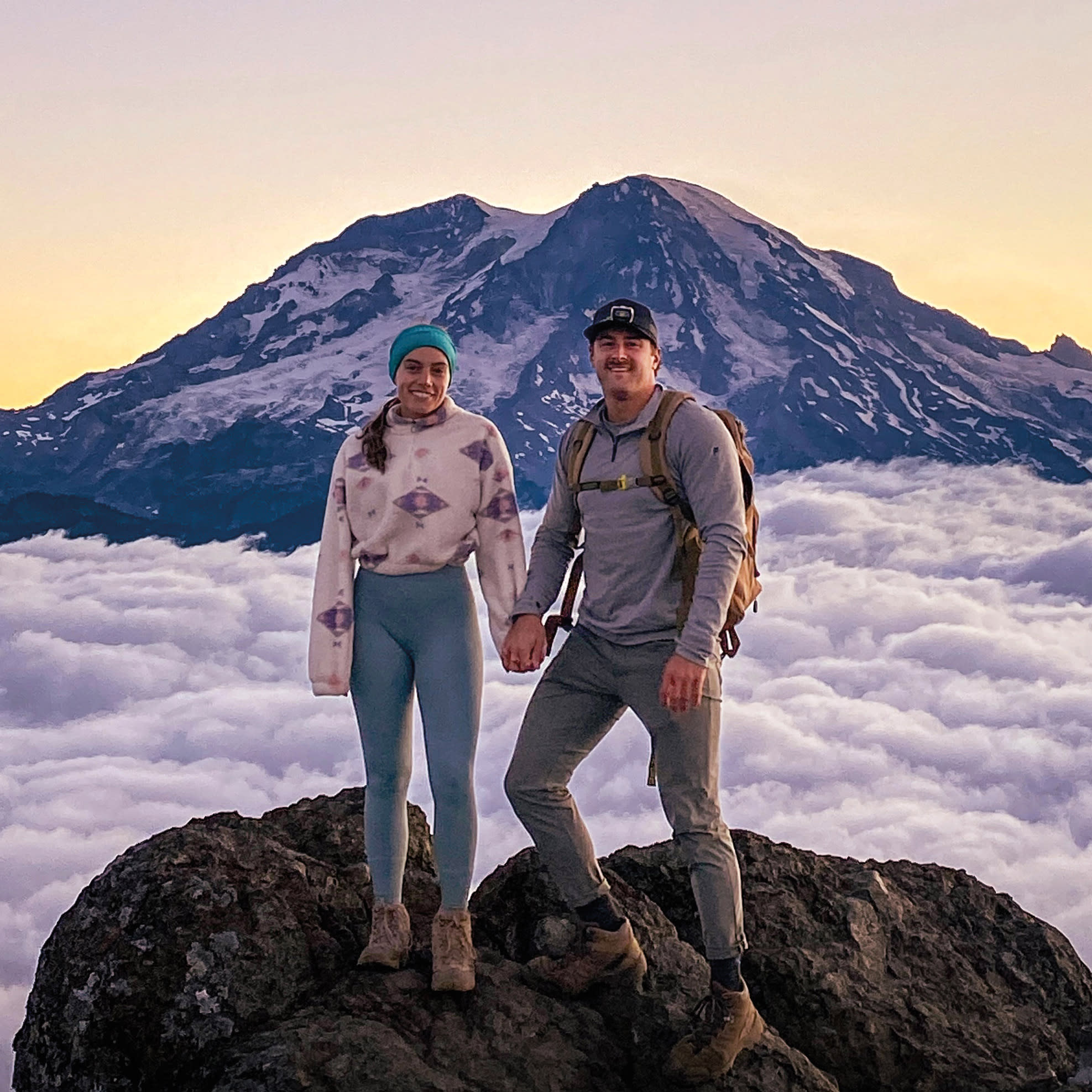 Cara Napolitano ’18 and Tristan Hollenbaugh ’18 standing atop Mount Rainier, with a snow-capped mountain and clouds behind them.