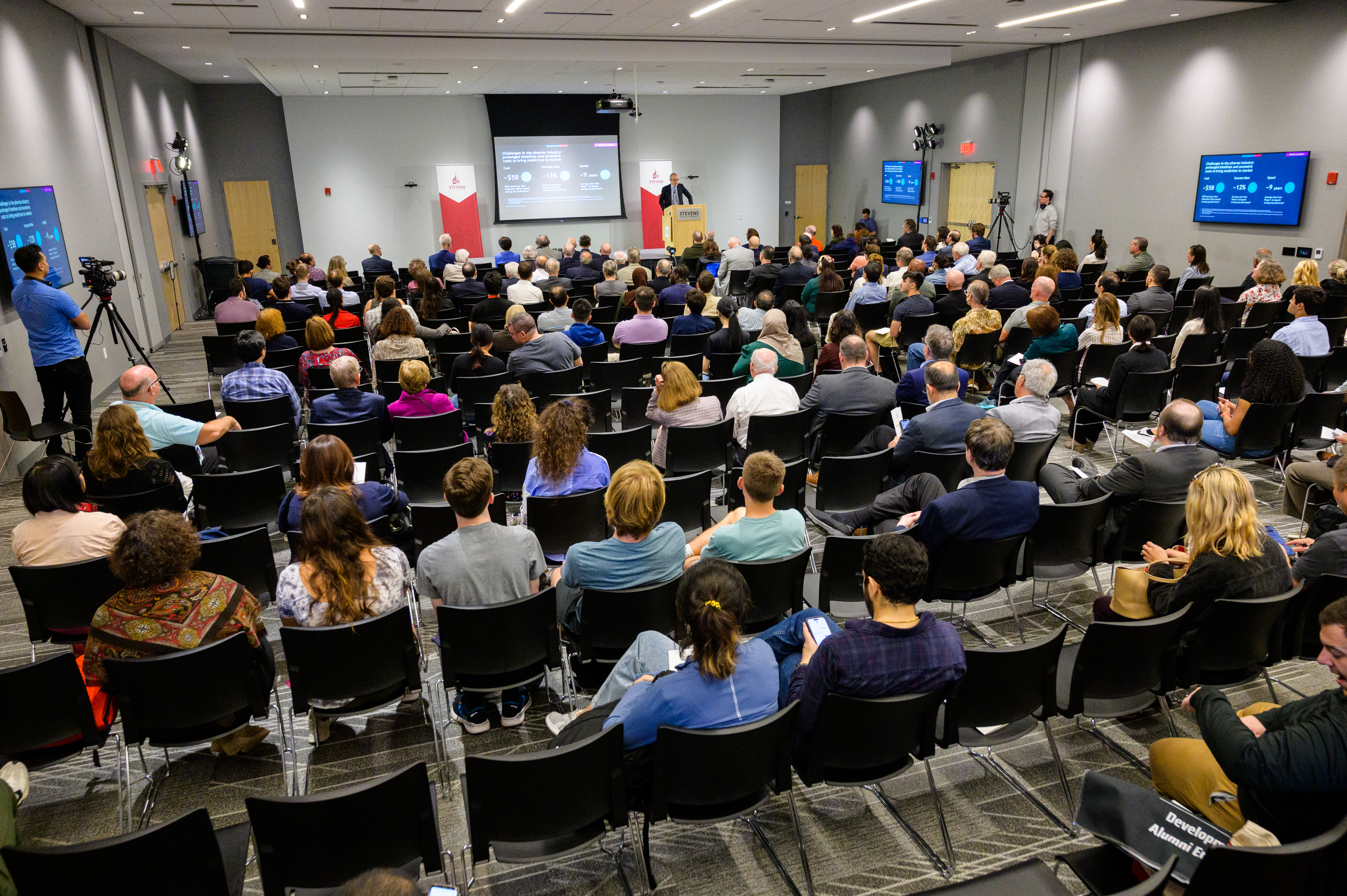 A full shot of a seated audience listening to a speaker give a presentation.