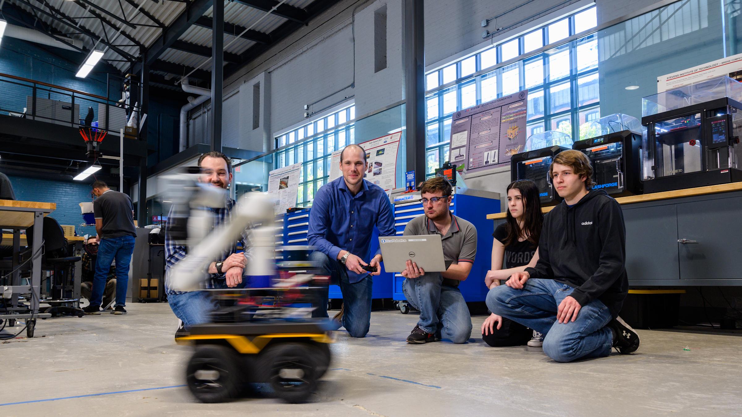 Students and professors gather on the floor to work on a robot