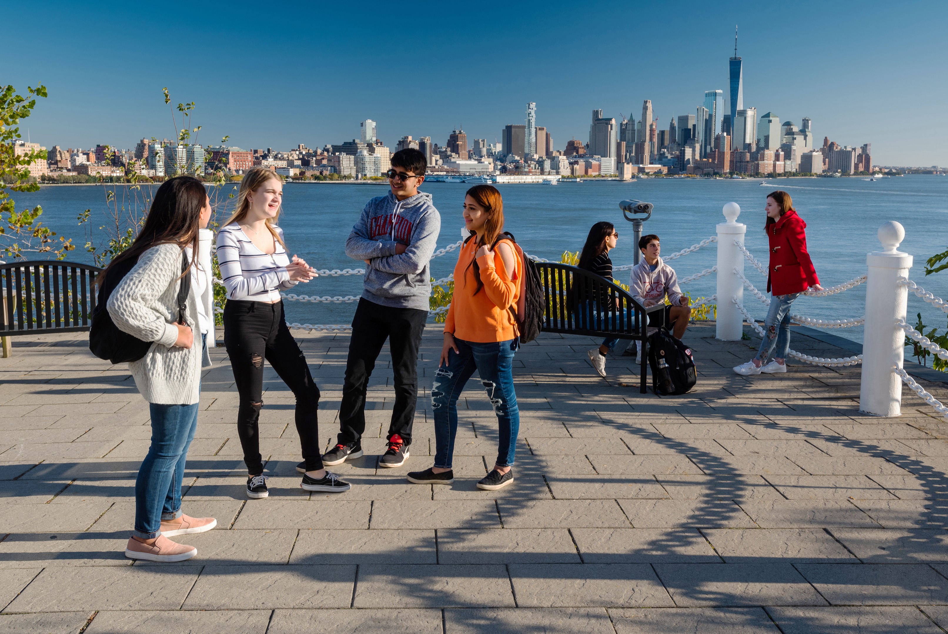 Students socialize at Castle Point with New York skyline in background.