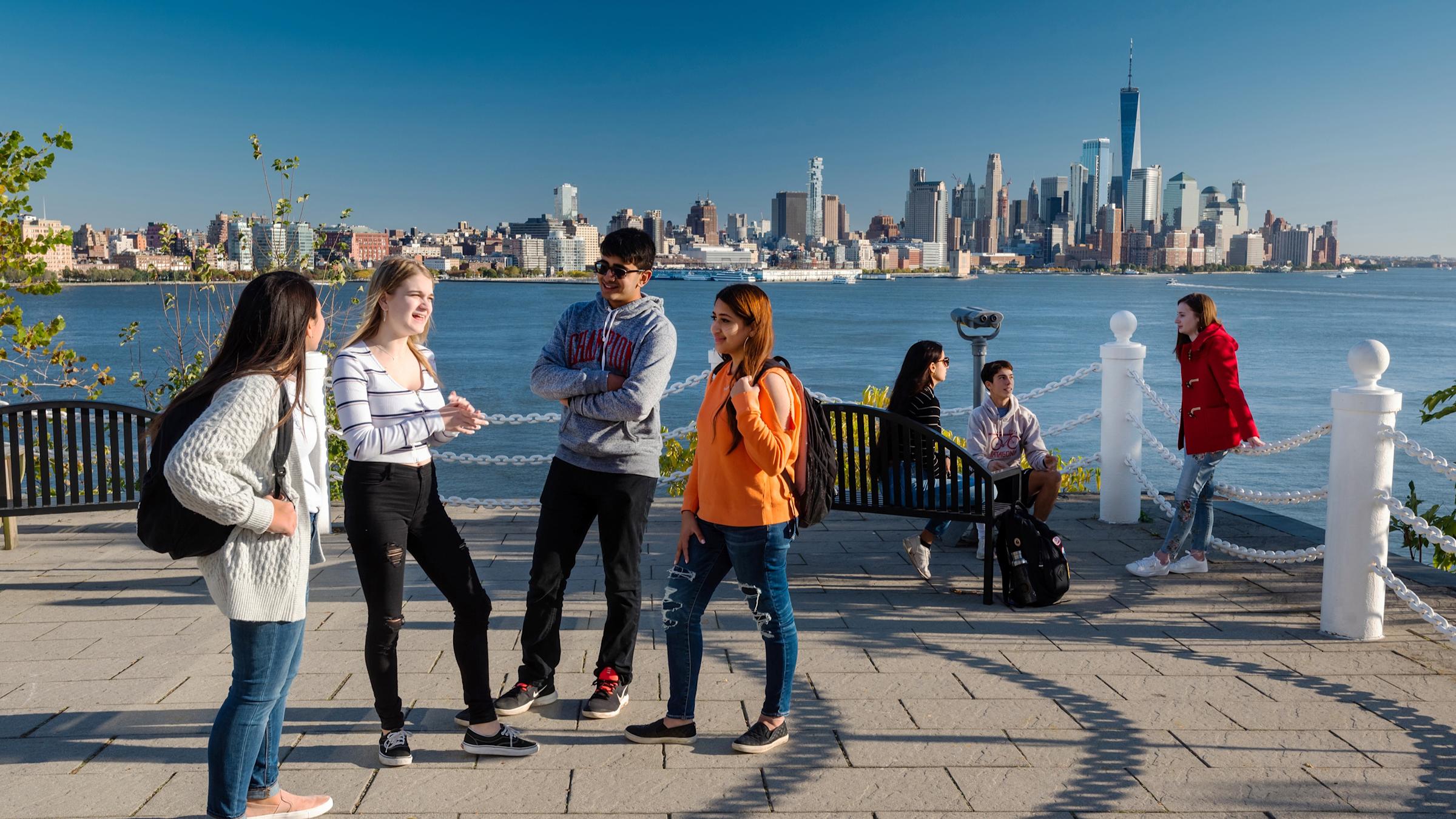 Students socialize at Castle Point with New York skyline in background.