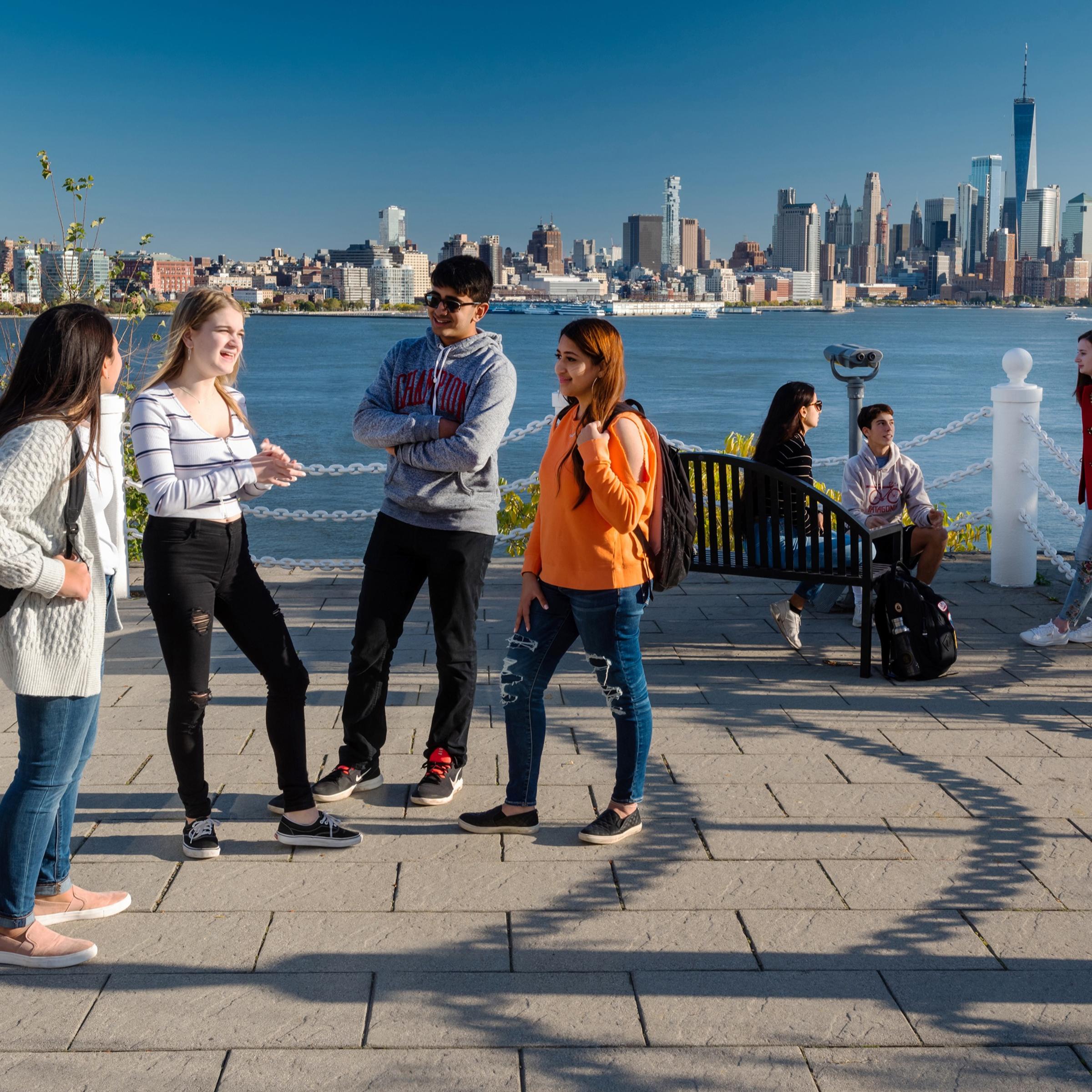 Students socialize at Castle Point with New York skyline in background.