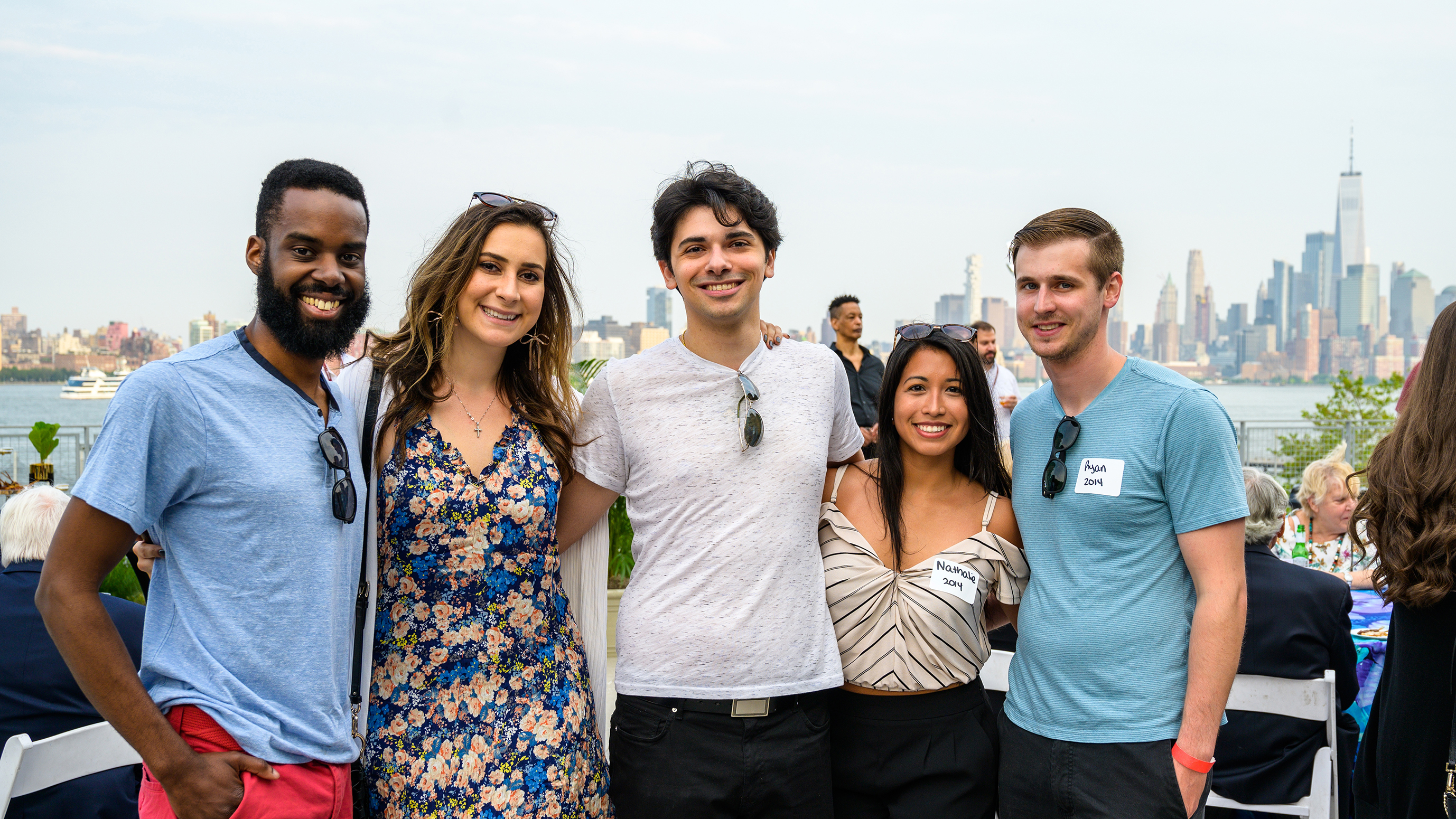 Five Stevens alumni pose for a photo outdoors in front of the New York skyline.