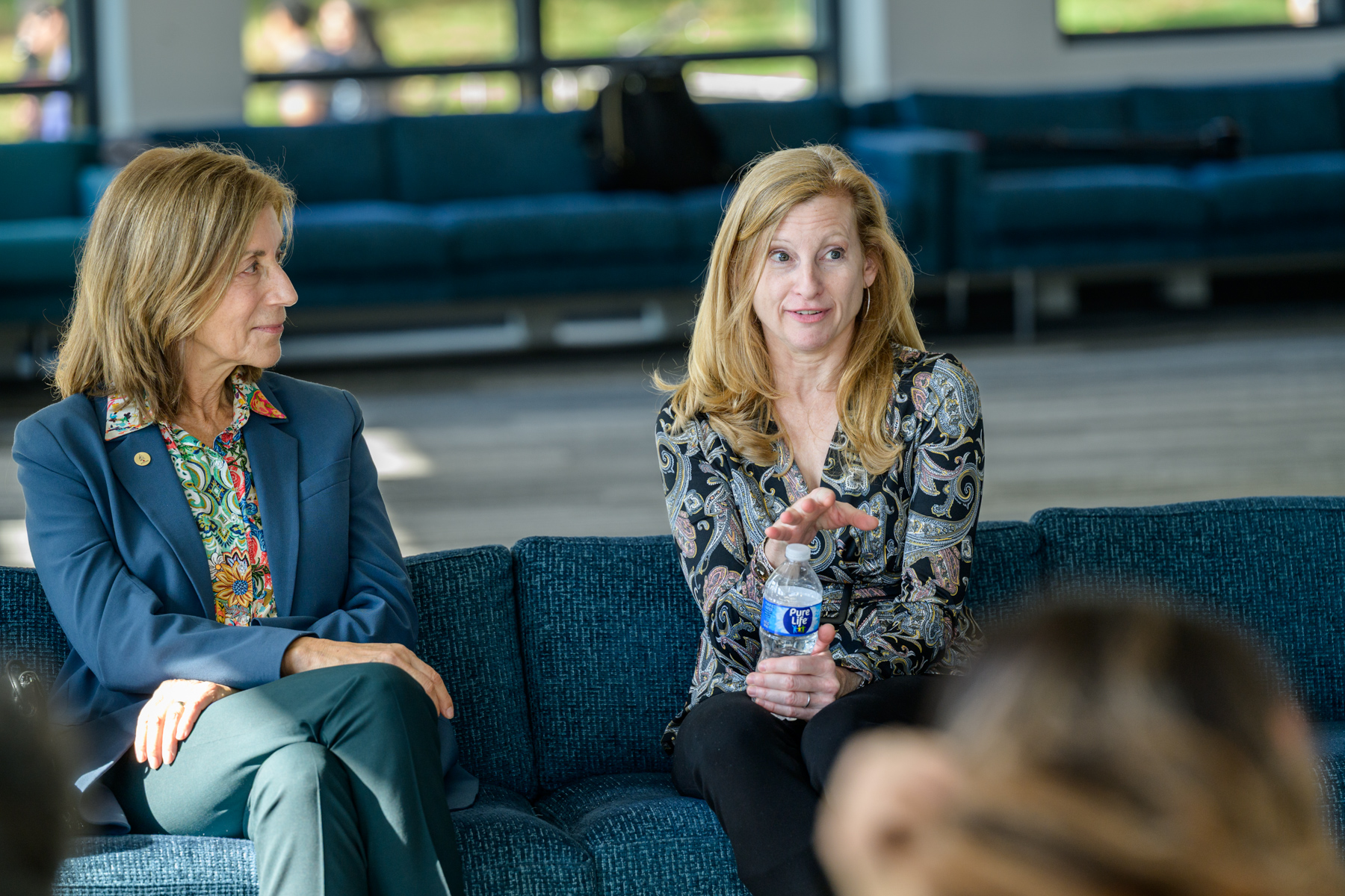 A woman sitting next to another woman speaks to a crowd.