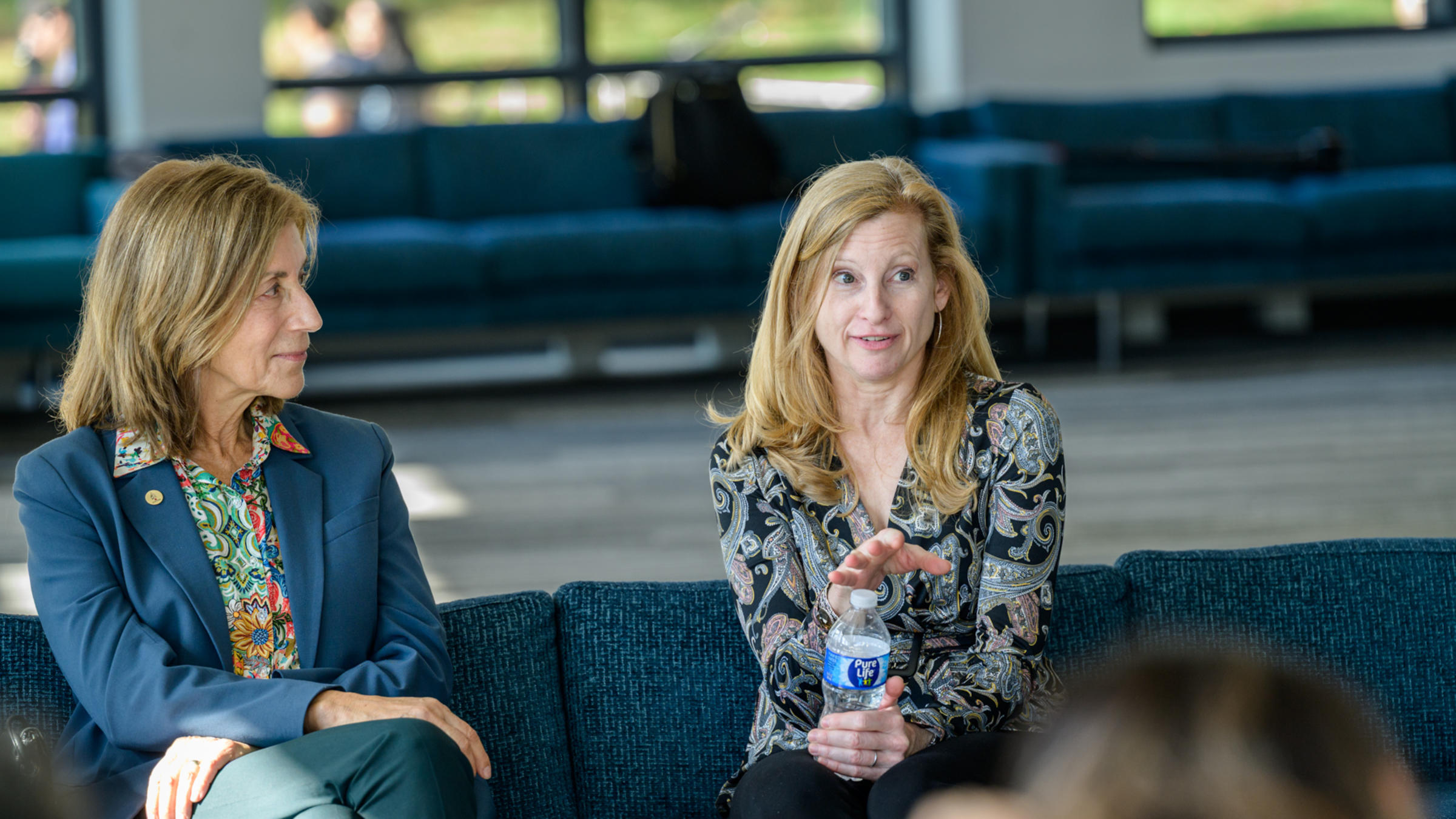 A woman sitting next to another woman speaks to a crowd.