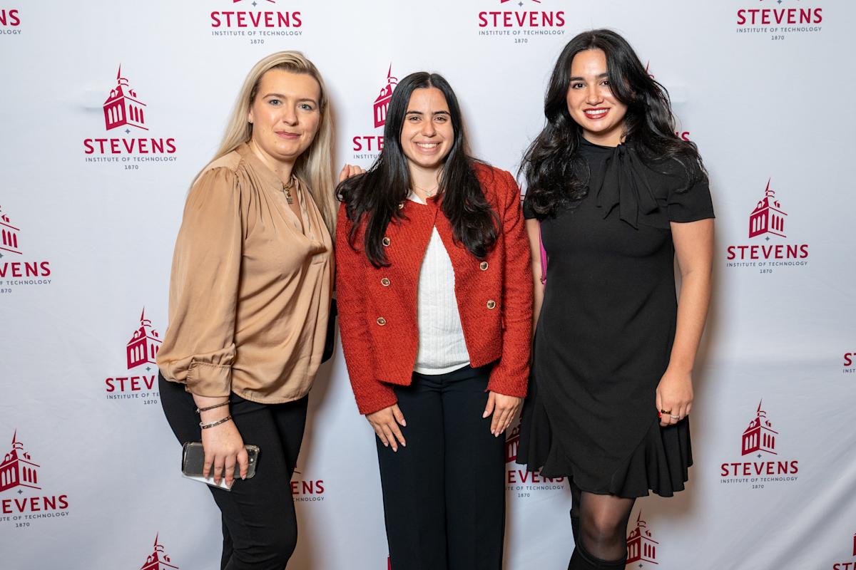 Three women stand in front of a Stevens step-and-repeat to pose for a photo