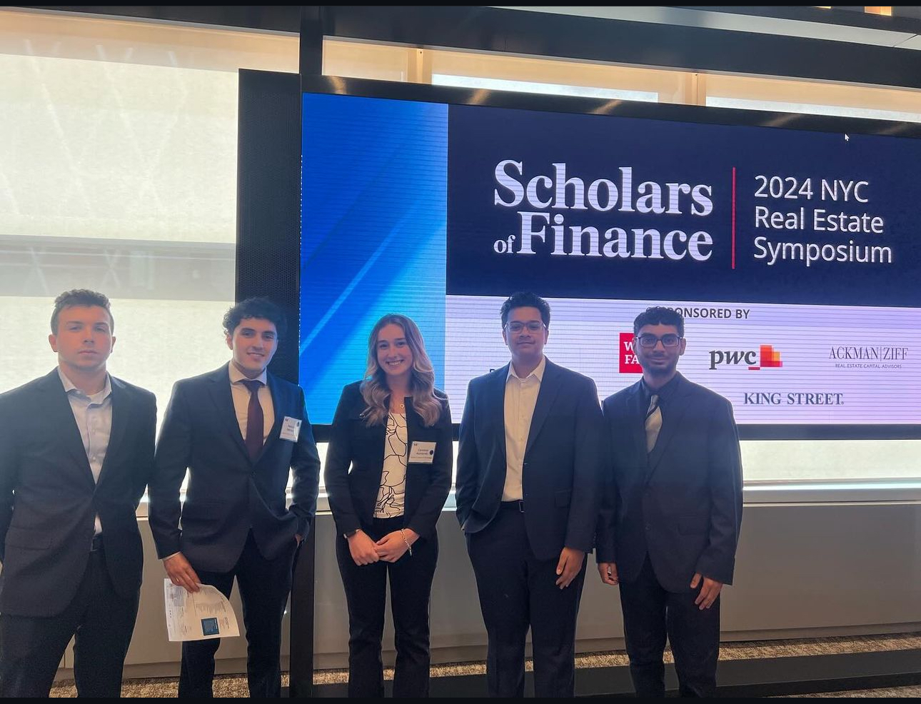 Five Stevens students stand in front of an LED wall with the Scholars of Finance logo.