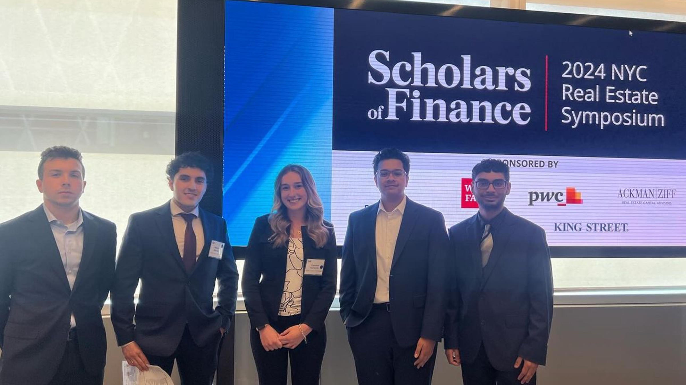 Five Stevens students stand in front of an LED wall with the Scholars of Finance logo.