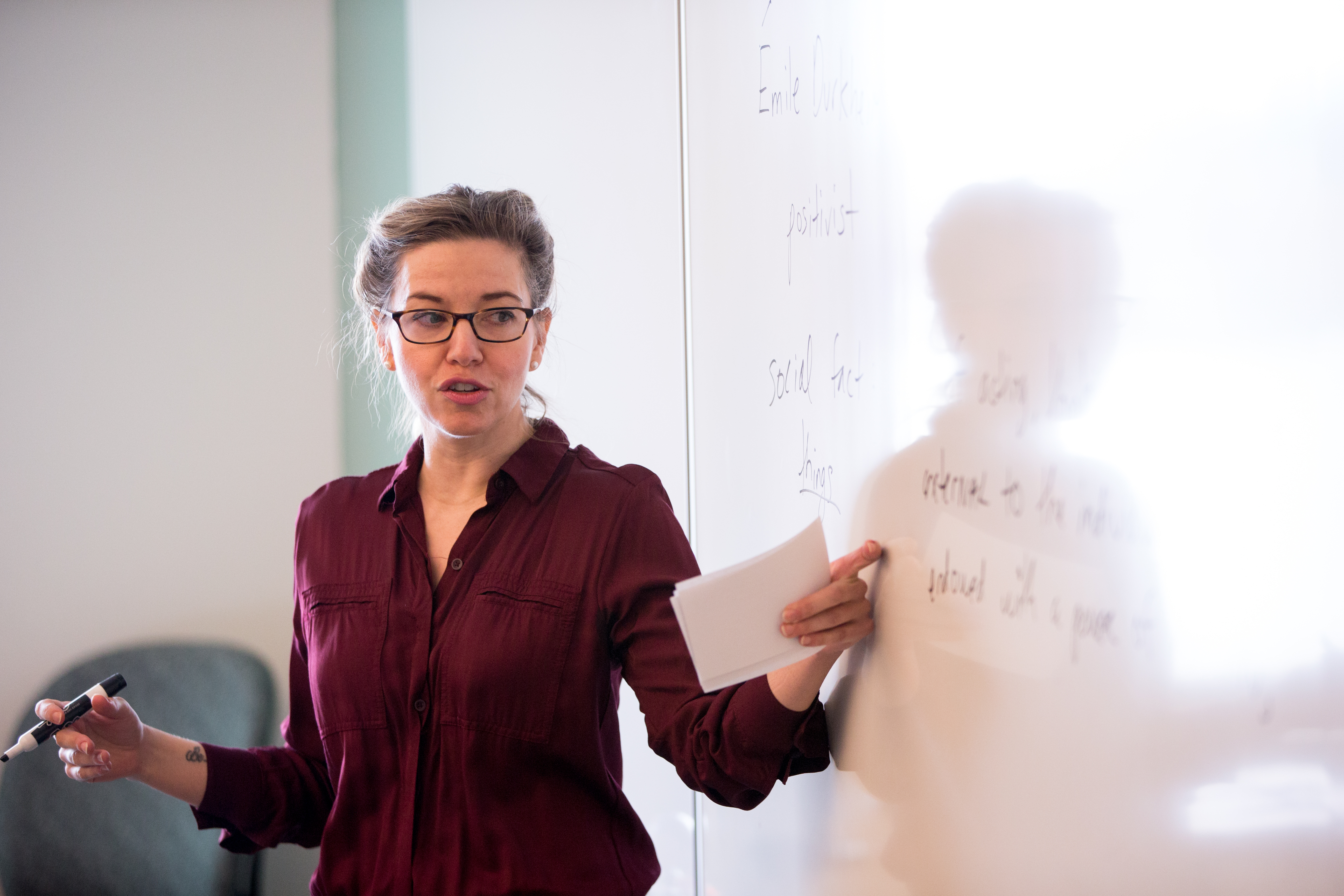 Professor in front of class gestures toward white board with sociology text written on it