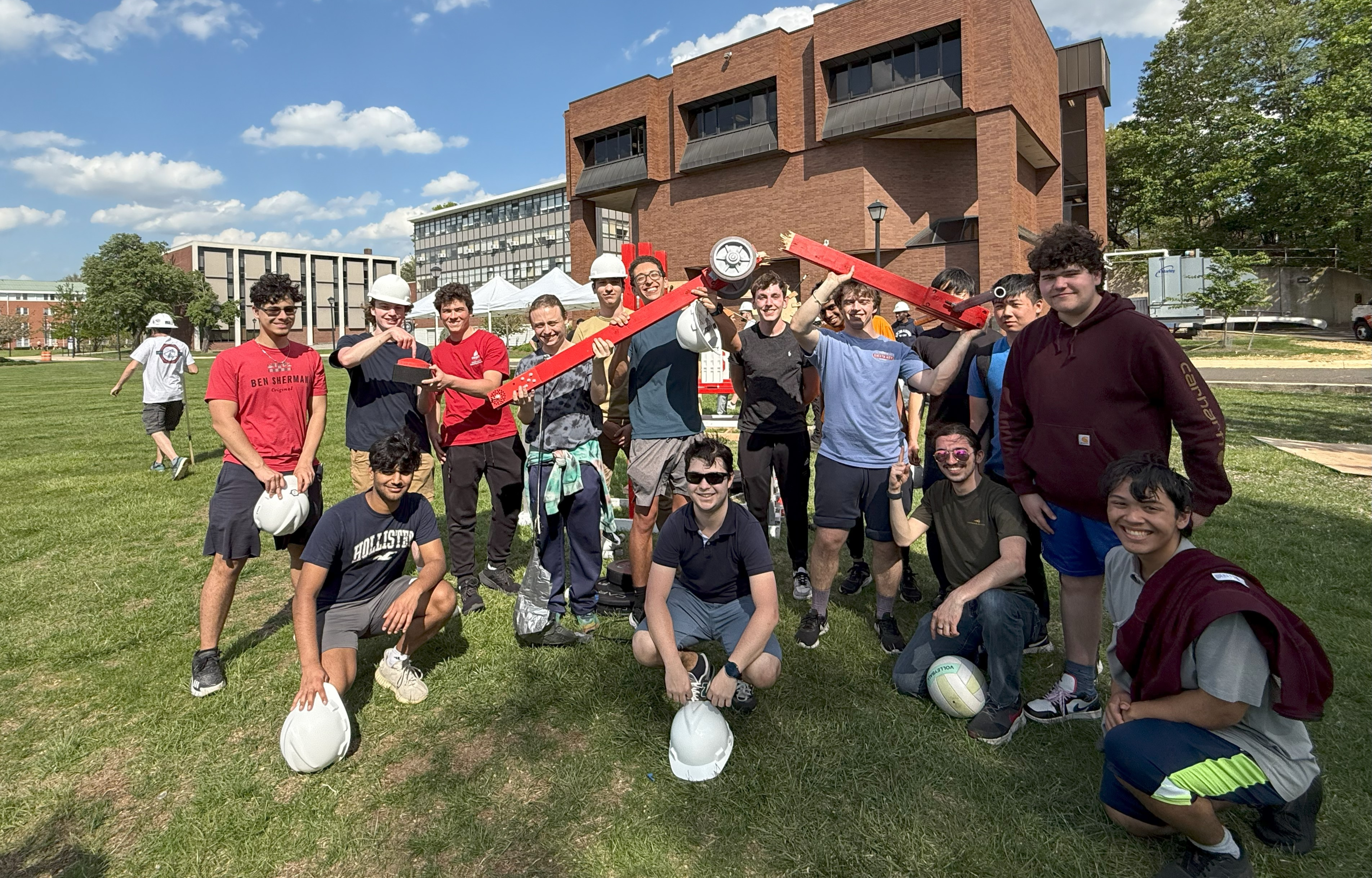 A group of students stand together smiling, holding up a long piece of wood that is broken in half.