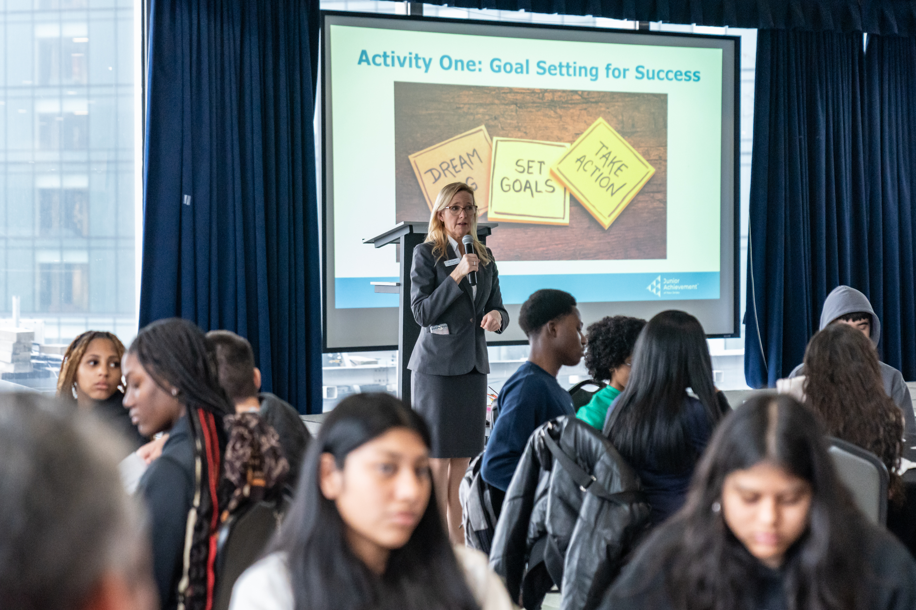 Christy Biedron, Vice President of Education of JANJ, holds a microphone while speaking in front of an audience.