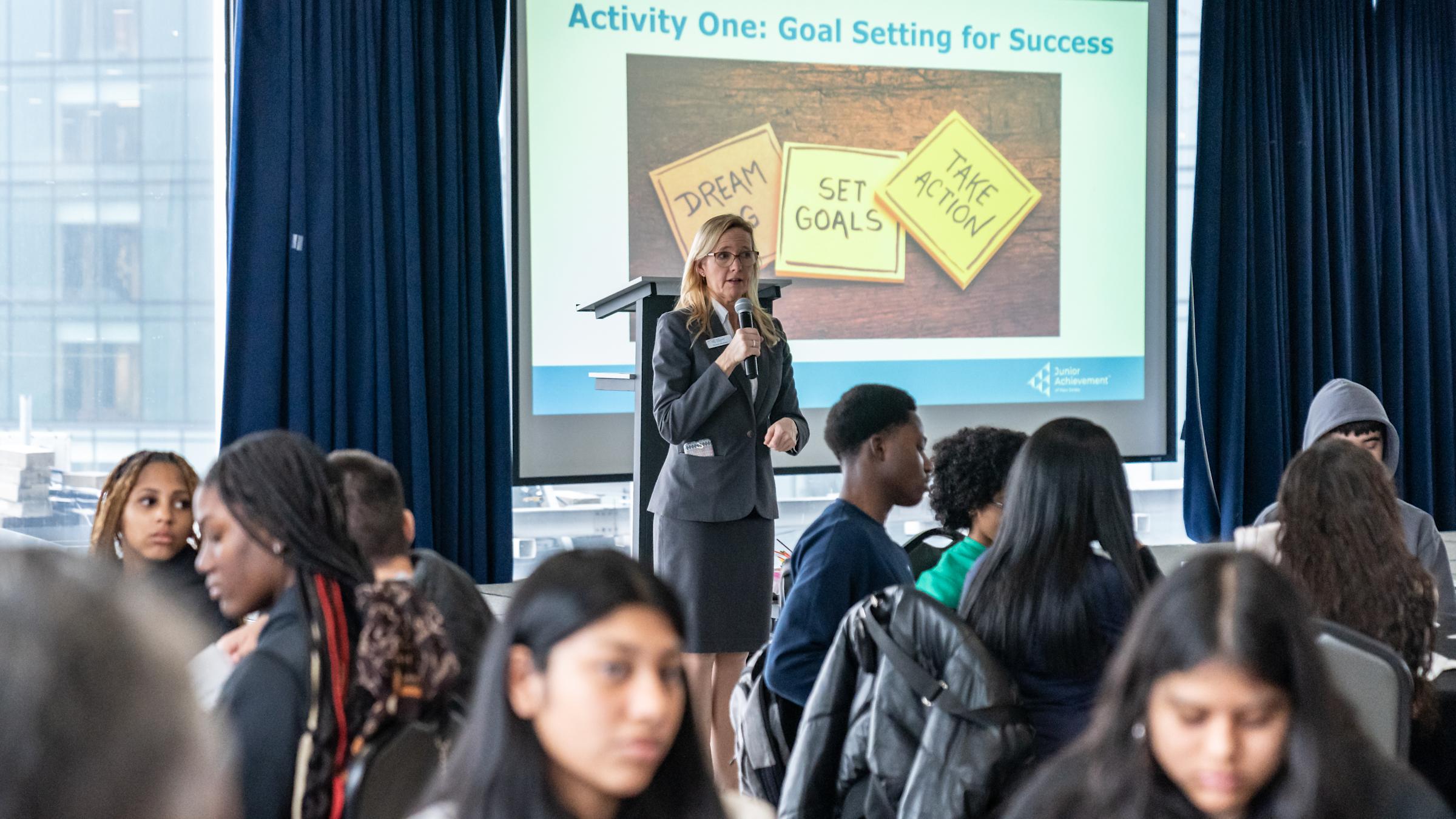 Christy Biedron, Vice President of Education of JANJ, holds a microphone while speaking in front of an audience.