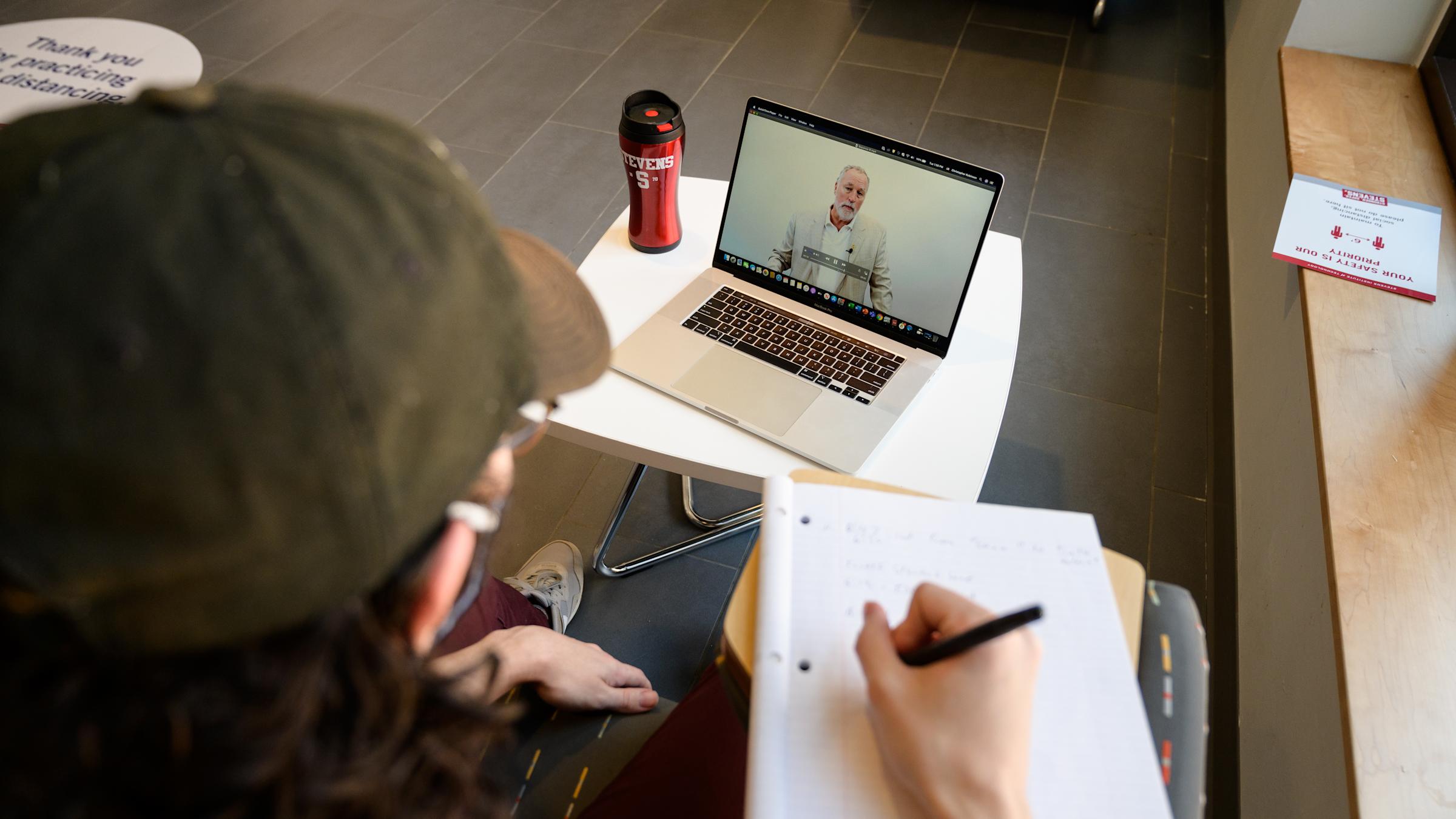 Student taking notes while watching an online lecture