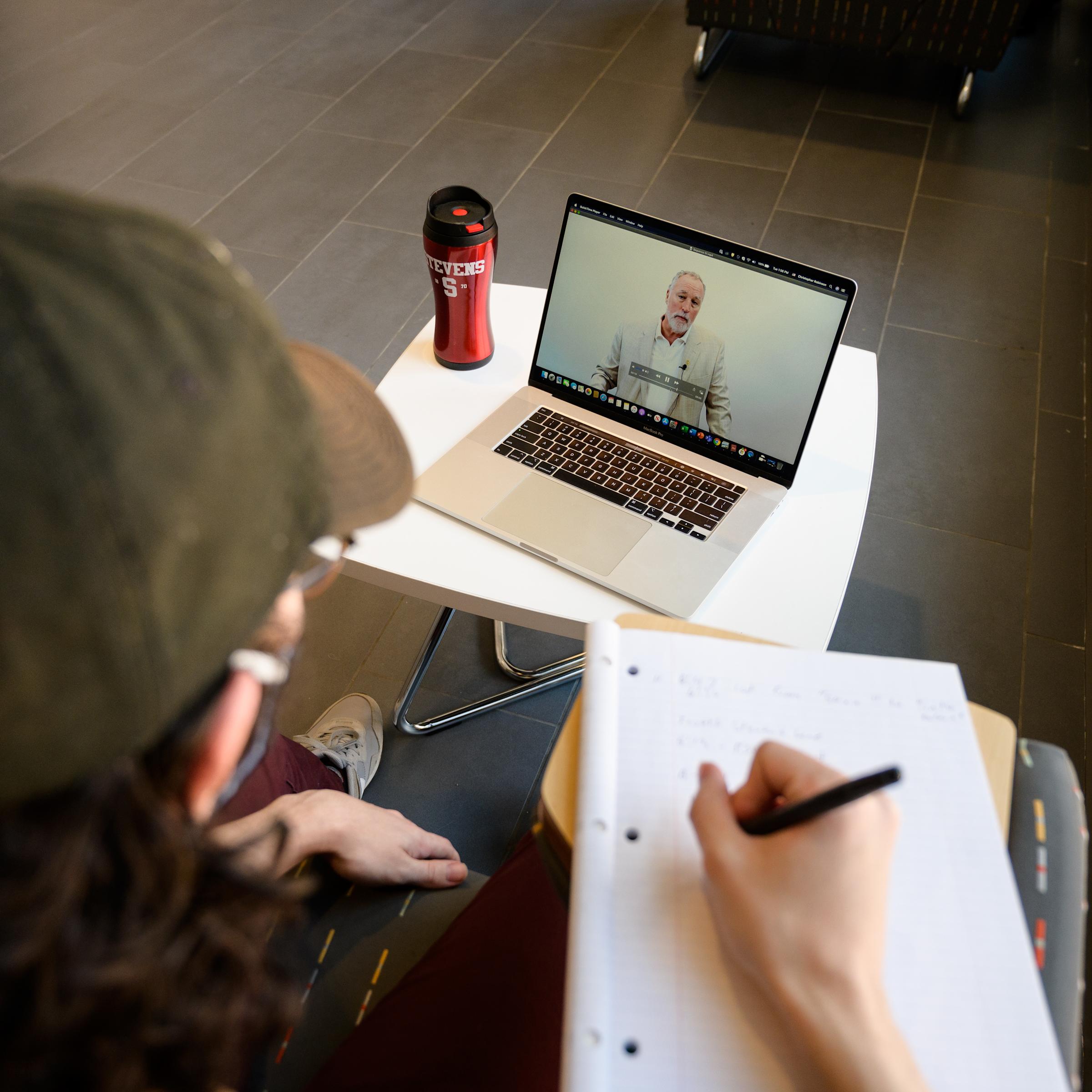 Student taking notes while watching an online lecture