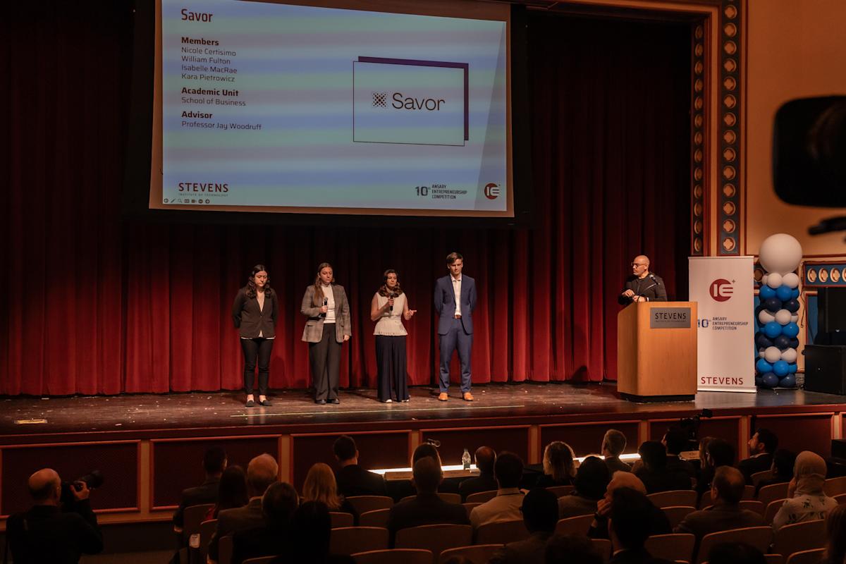 Four students stand on a stage presenting their project. 