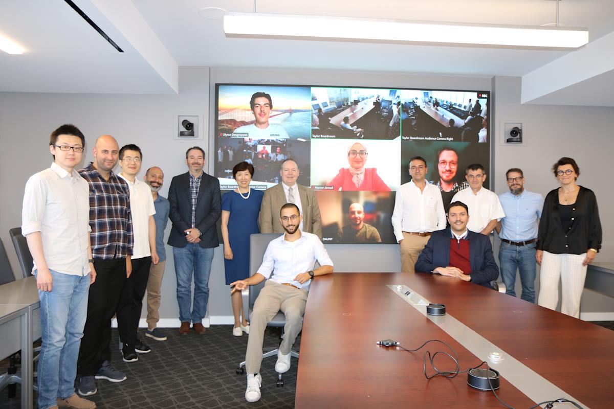 A group of Stevens leadership, students and a delegation of École Centrale de Nantes (ECN) leaders pose in front of a monitor of other participants. 