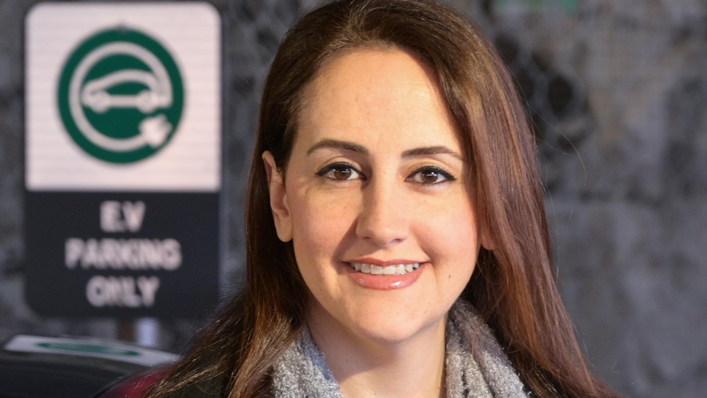 A headshot of Yeganeh Hayeri in front of an electric vehicle sign