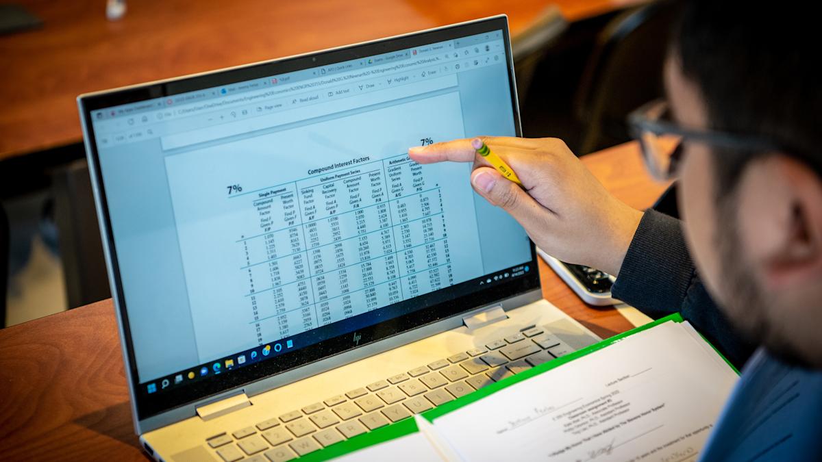 Student points to laptop screen showing a spreadsheet