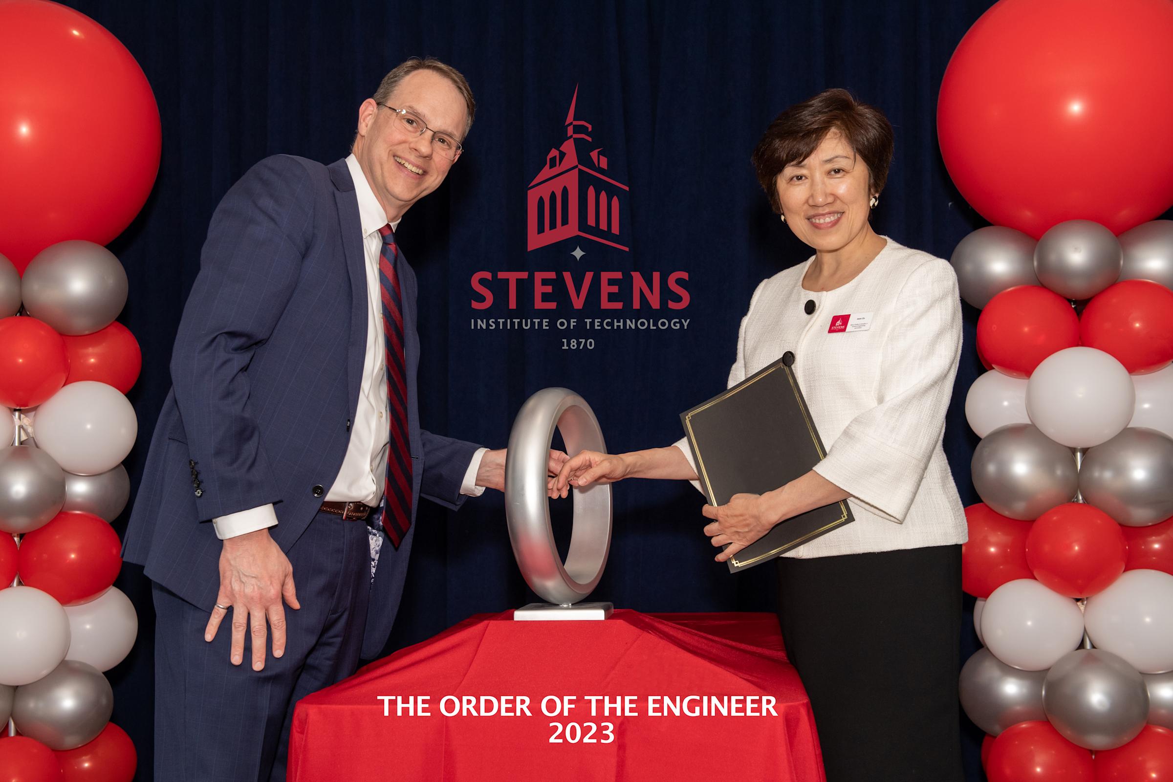 Steven Schriener (left) and Dean Jean Zu (right), as Schriener puts ring on Zu's finger through large metal "ring"